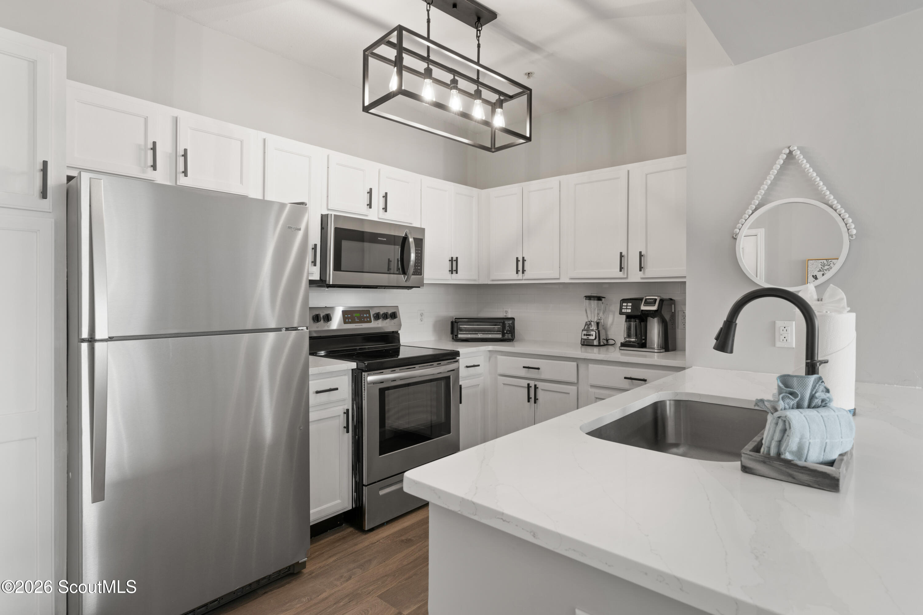 Modern kitchen with white cabinets, stainless steel appliances, and a marble-look peninsula with a black faucet.