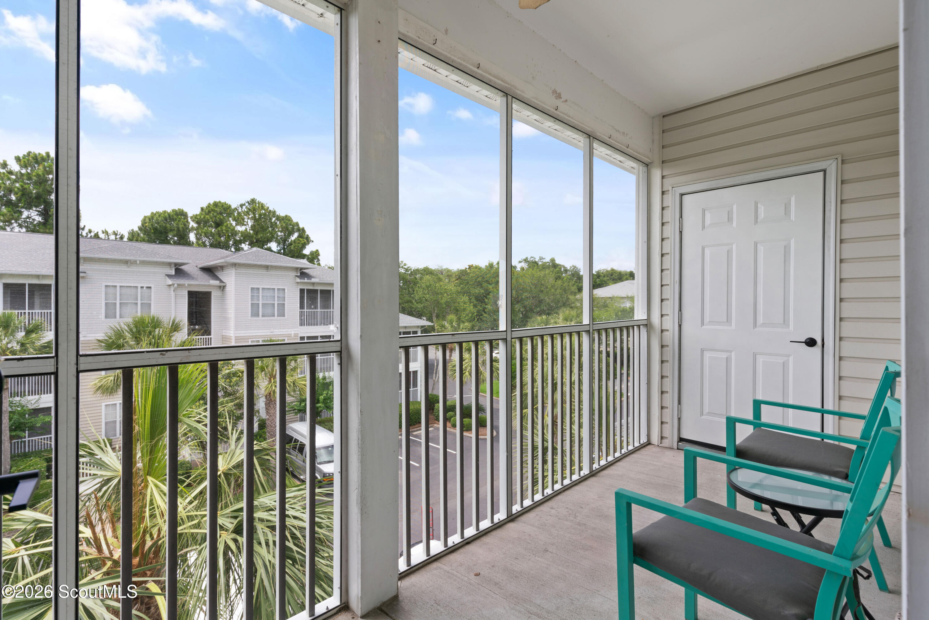 Screened balcony with teal chairs and a glass table overlooking palm trees and neighboring homes.