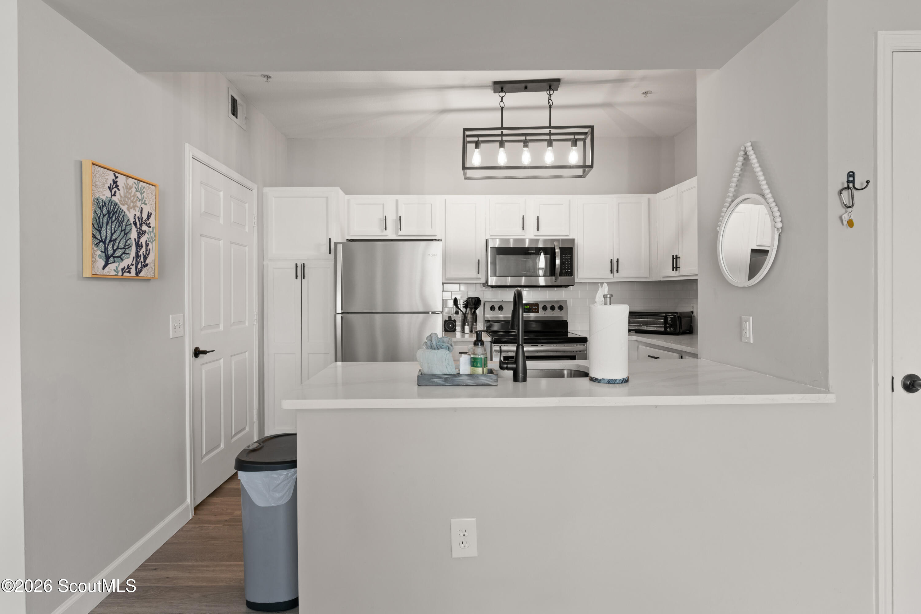 Modern white kitchen with stainless steel appliances and a peninsula with a black faucet.