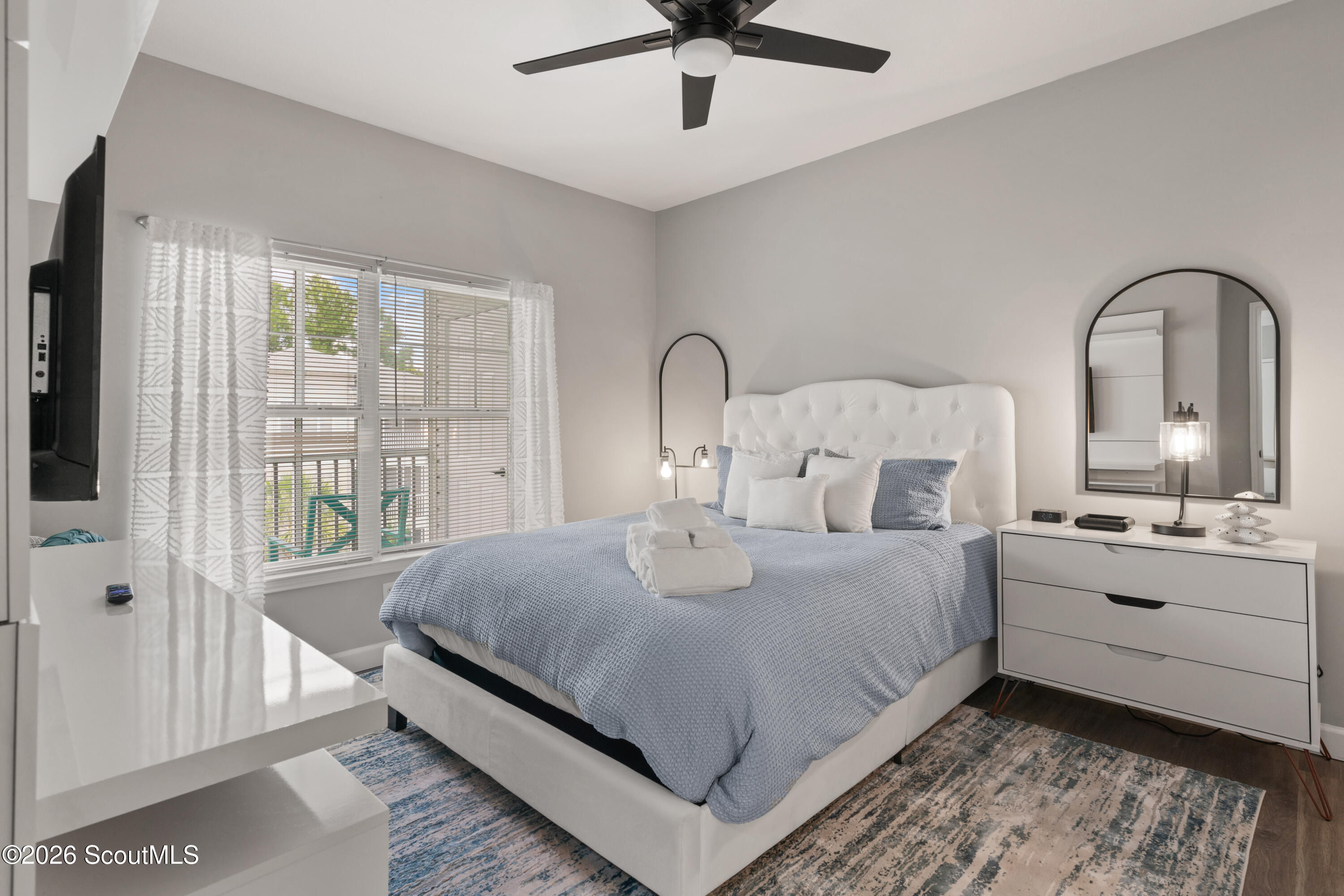 Staged bedroom with a large blue-gray bed, tufted white headboard, and arched mirror above a dresser.