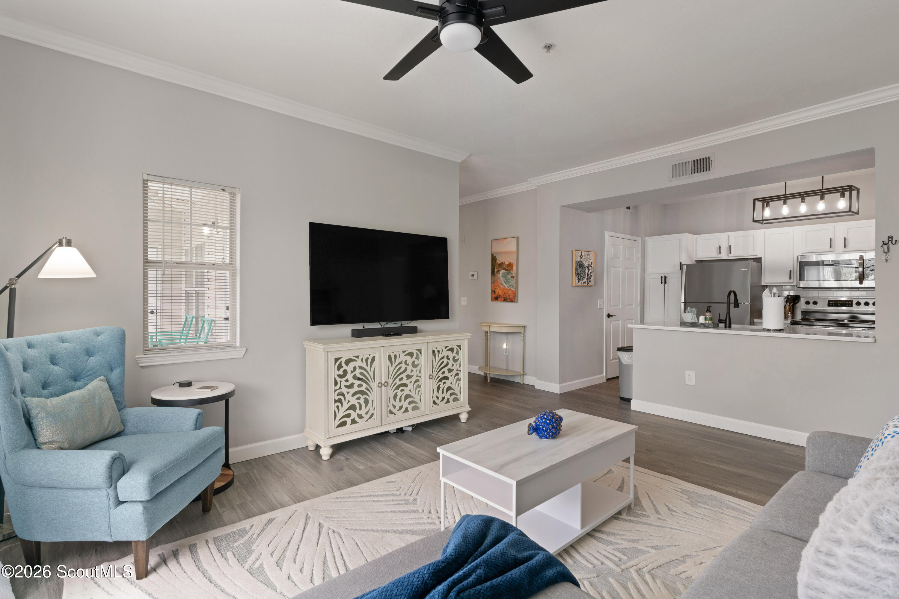 Furnished living room with a blue armchair, patterned rug, and open kitchen.