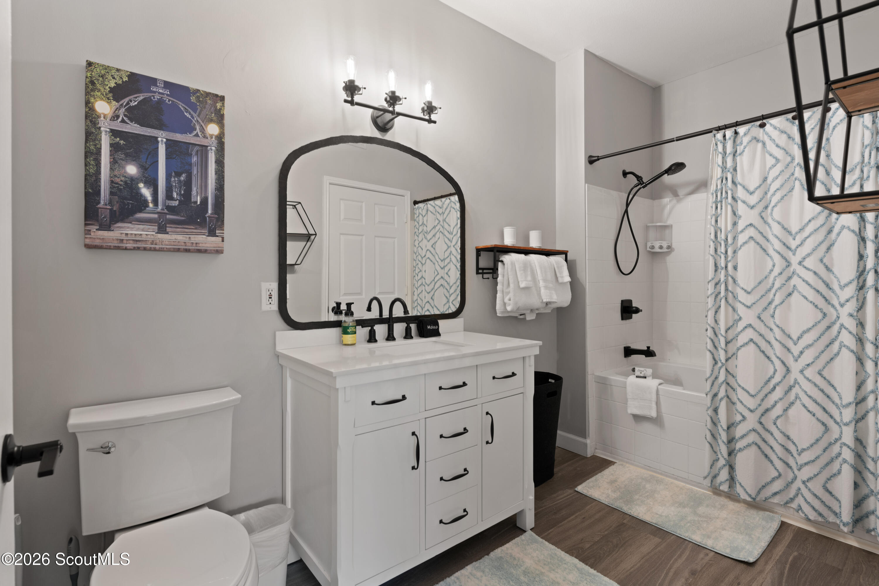 Bathroom with a white vanity, arched mirror, and tub behind a blue geometric shower curtain.