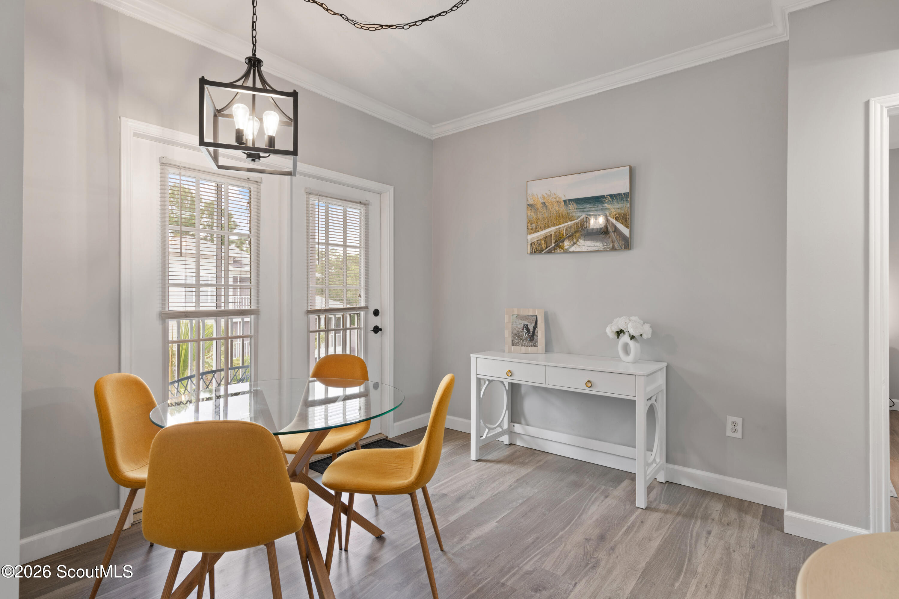 Dining area with a glass table, mustard-yellow chairs, and tall windows with blinds.