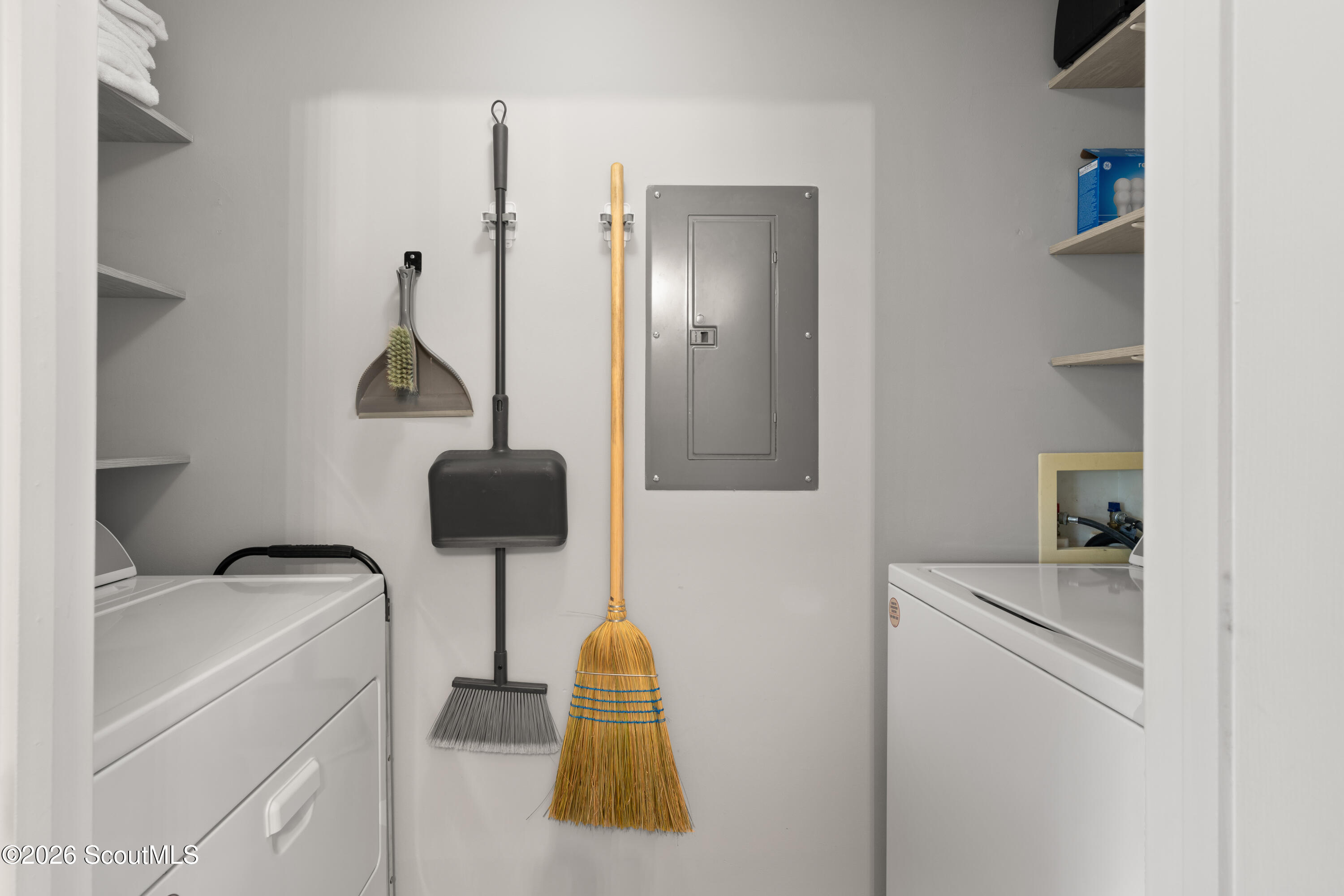 Laundry room with a washer and dryer, open shelves, and a broom and dustpan hanging on the wall.