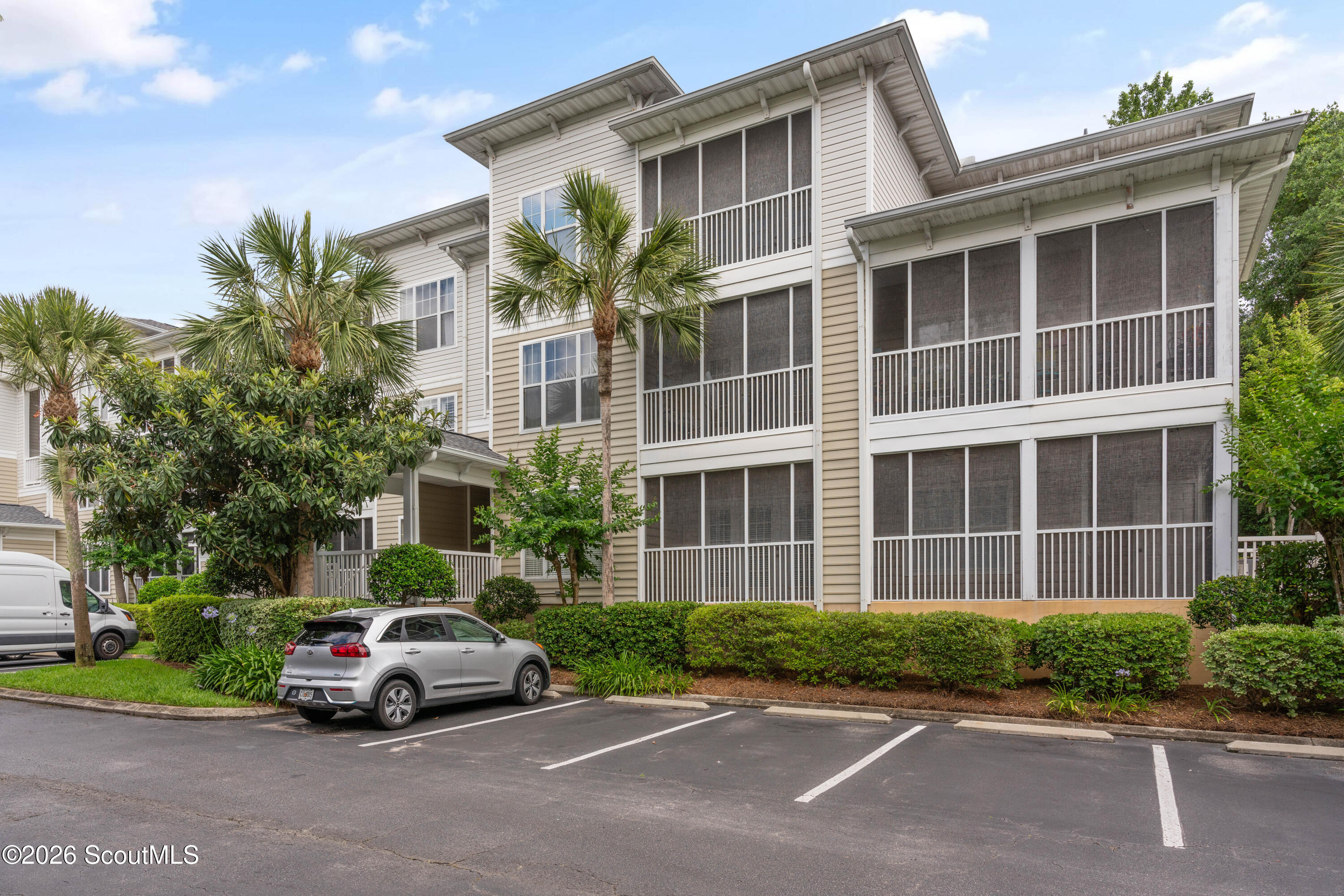 Multi-story condominium with screened balconies, palm trees, and a parking lot.