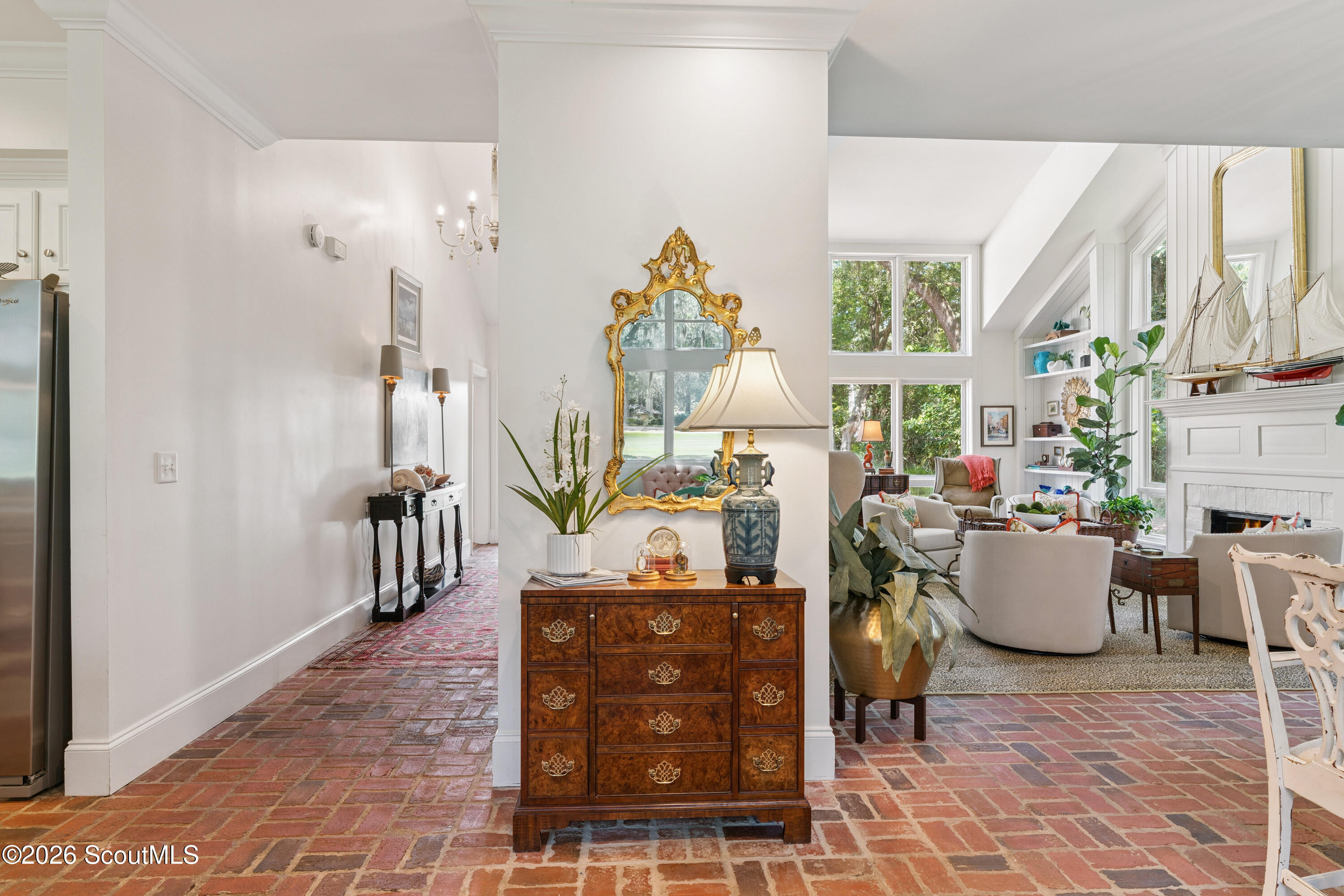 Furnished home interior with brick floors, an ornate gold mirror, and a bright living room with fireplace.