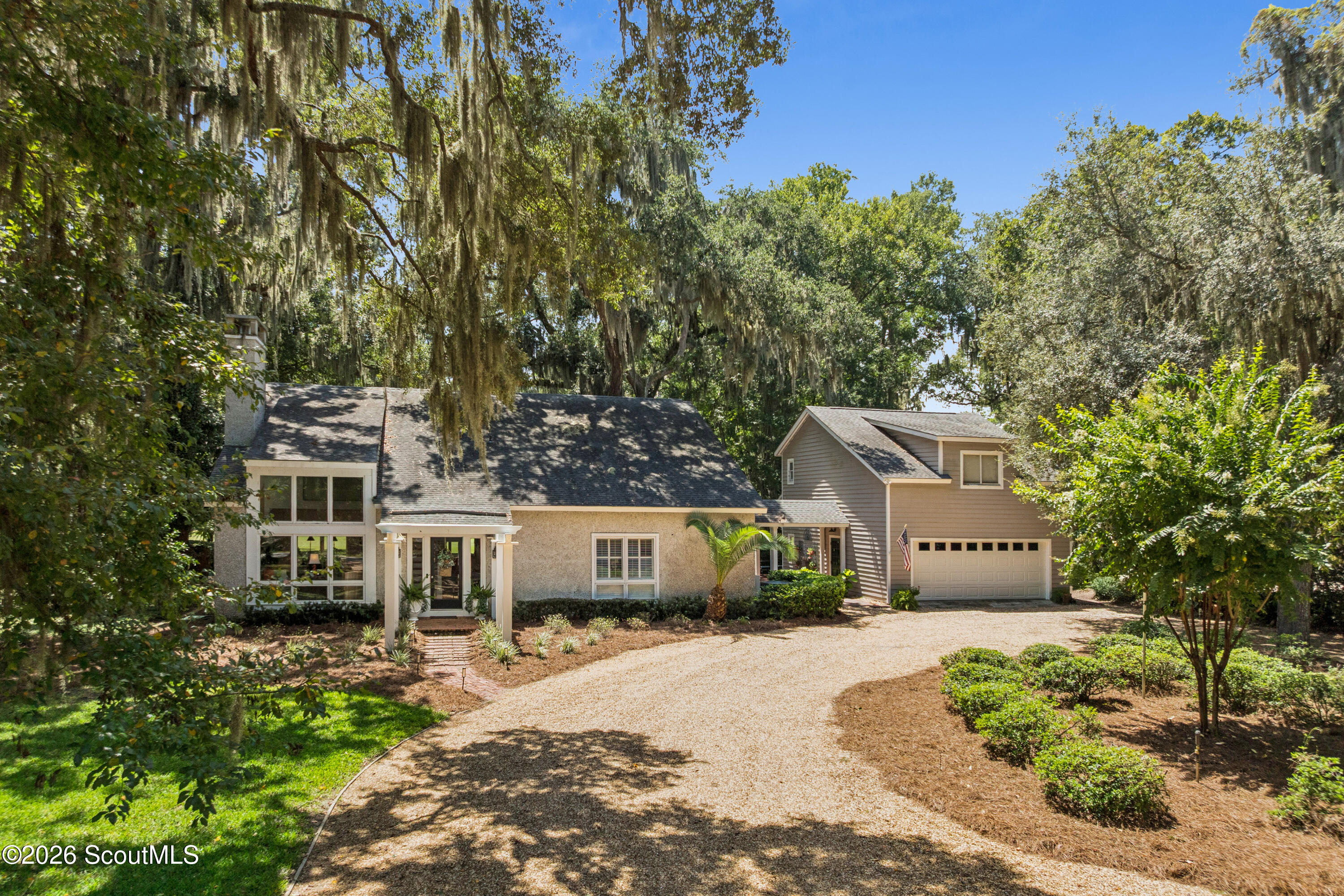 Home with attached garage and gravel driveway beneath mature Spanish moss-draped trees.