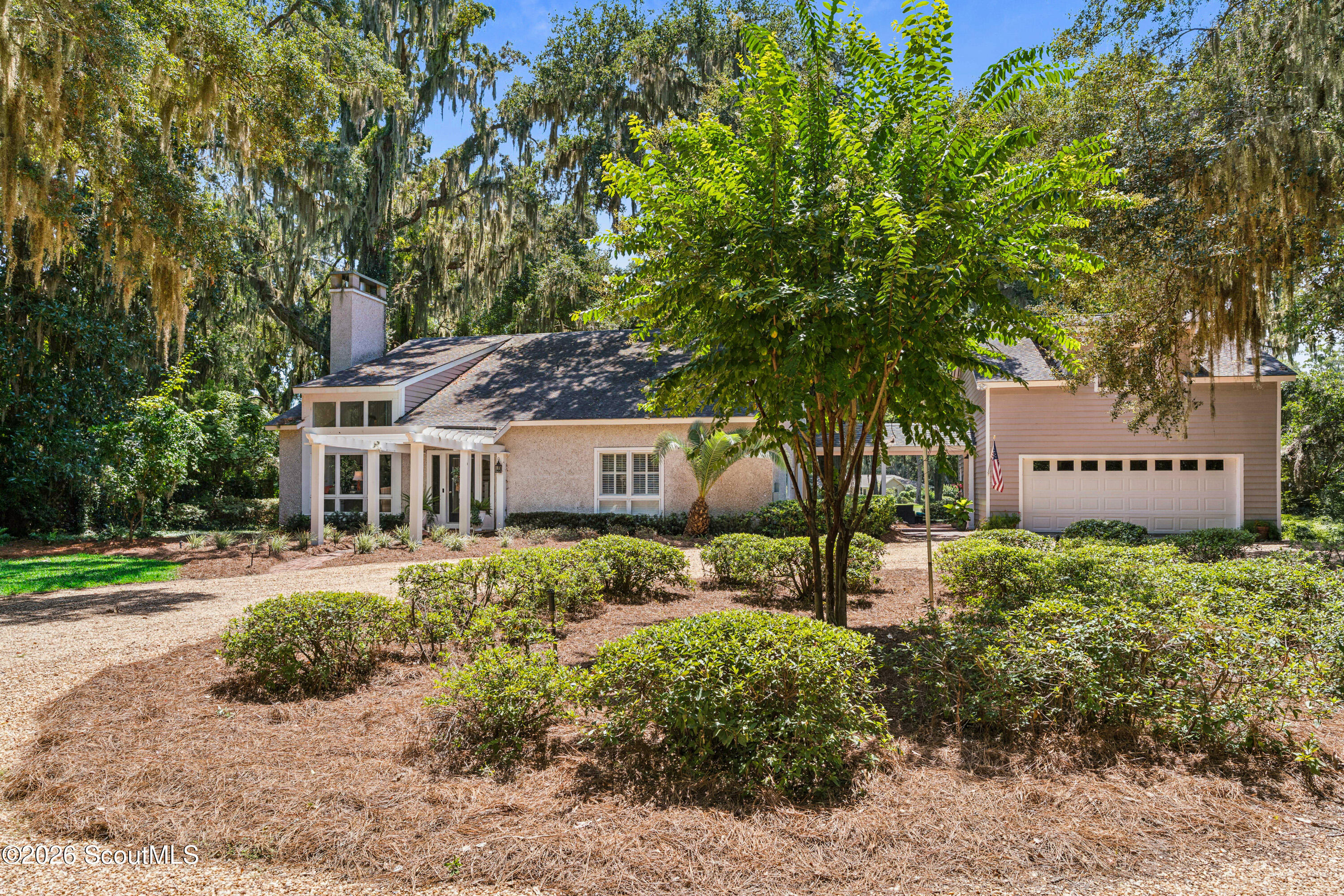 Single-story home with an attached garage, partly screened by a leafy tree and surrounded by mature moss-draped trees.