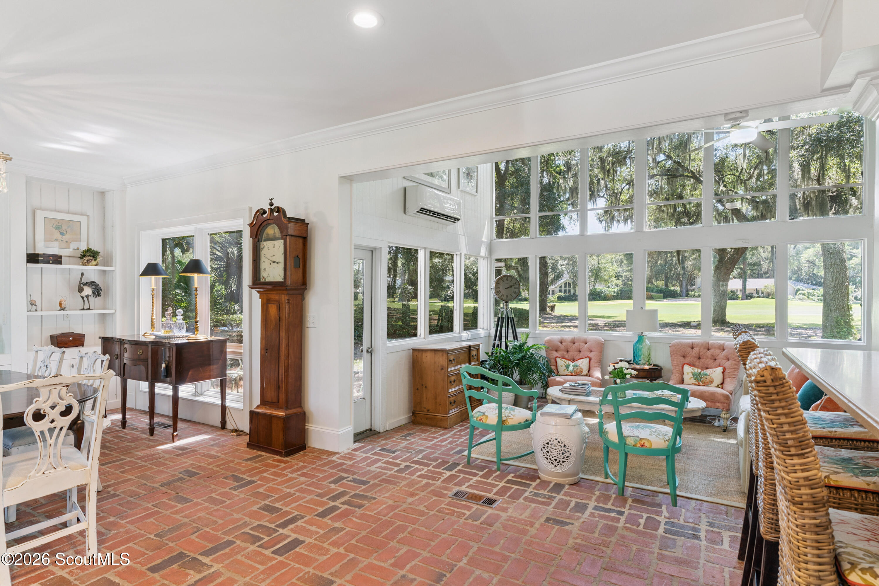 Furnished sunroom with a brick floor, tall windows, and views of a leafy lawn.