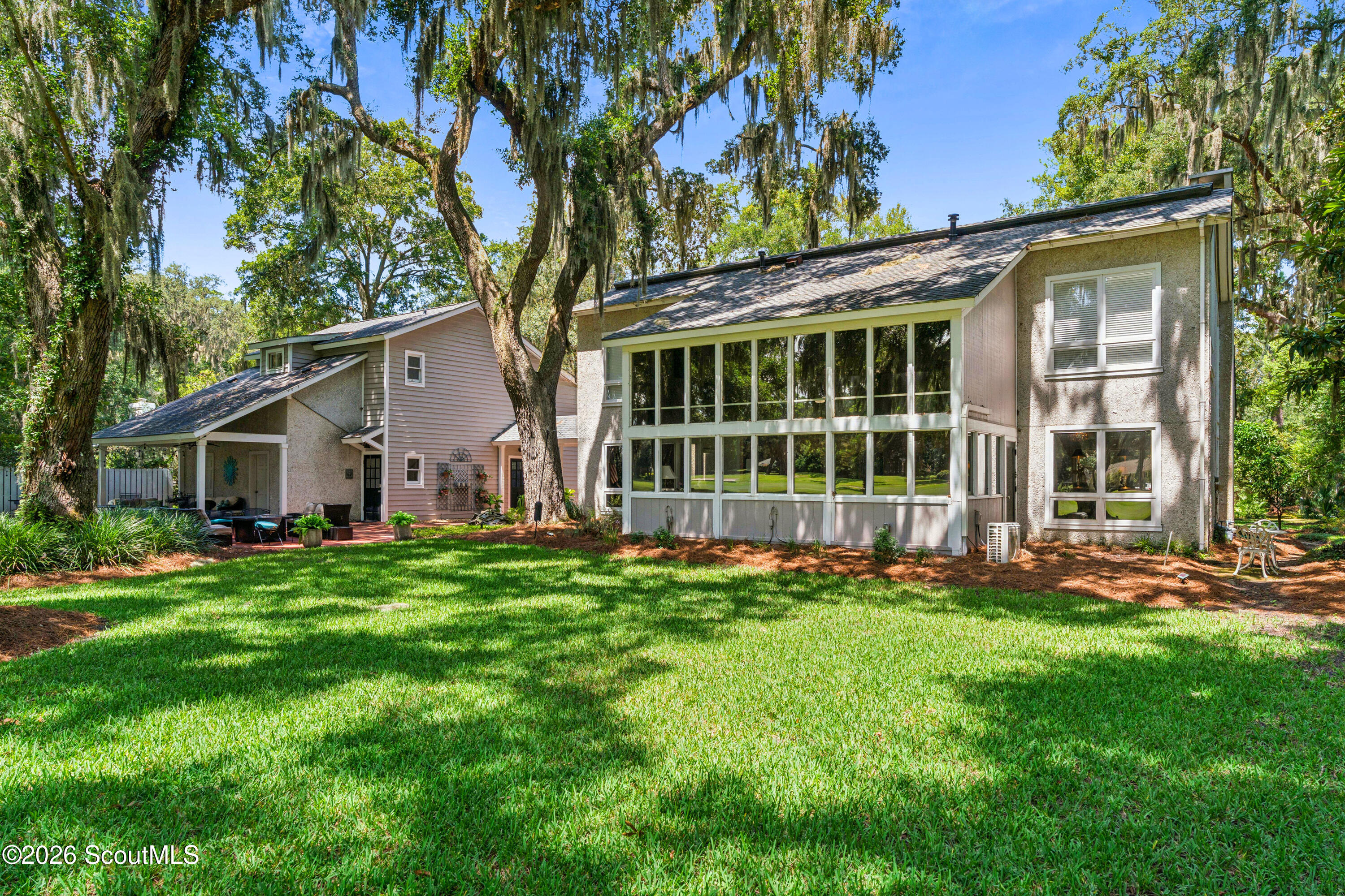 Two-story home with an expansive windowed sunroom, covered patio, and shady lawn beneath moss-draped trees.