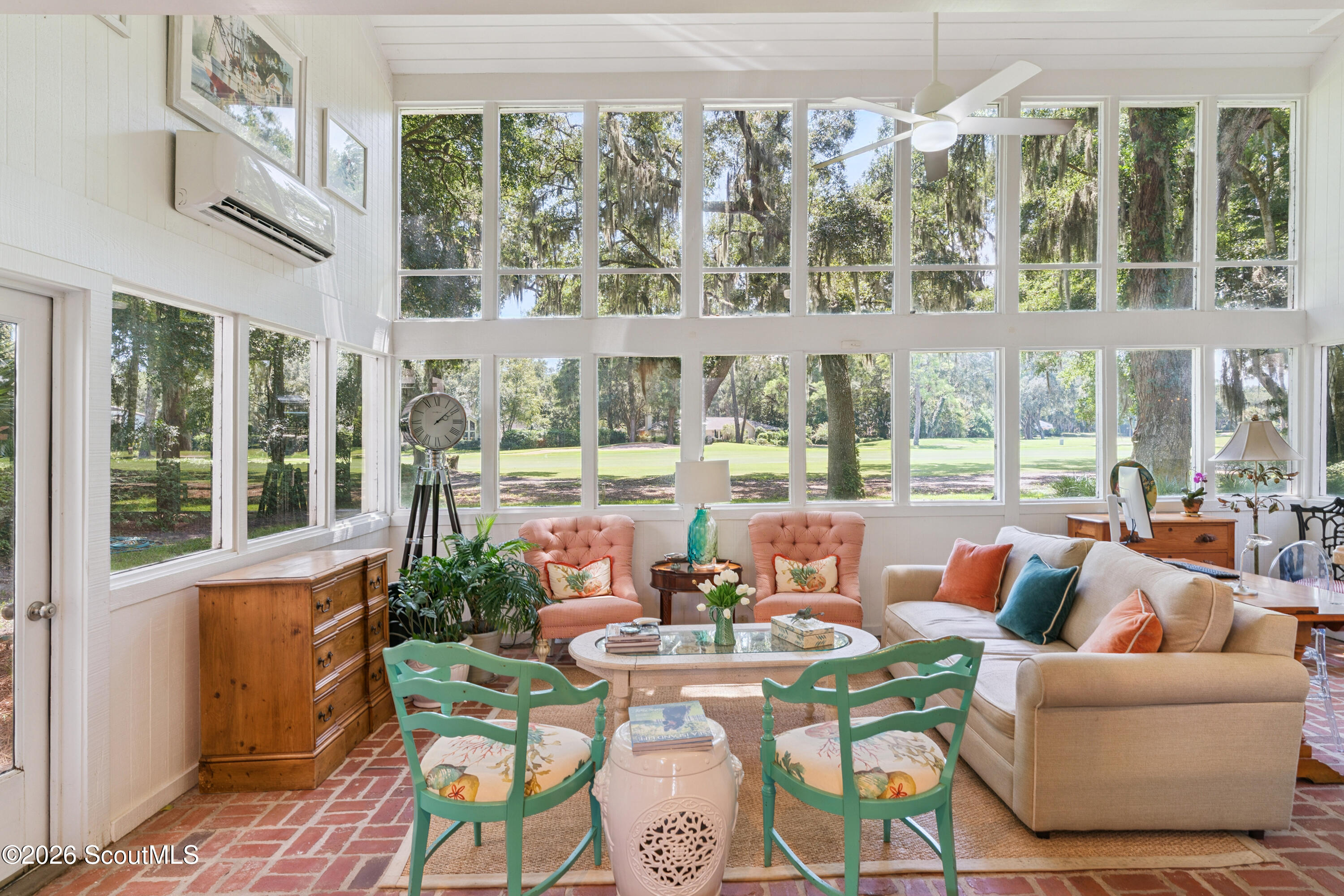 Furnished sunroom with floor-to-ceiling windows overlooking a tree-lined golf course.