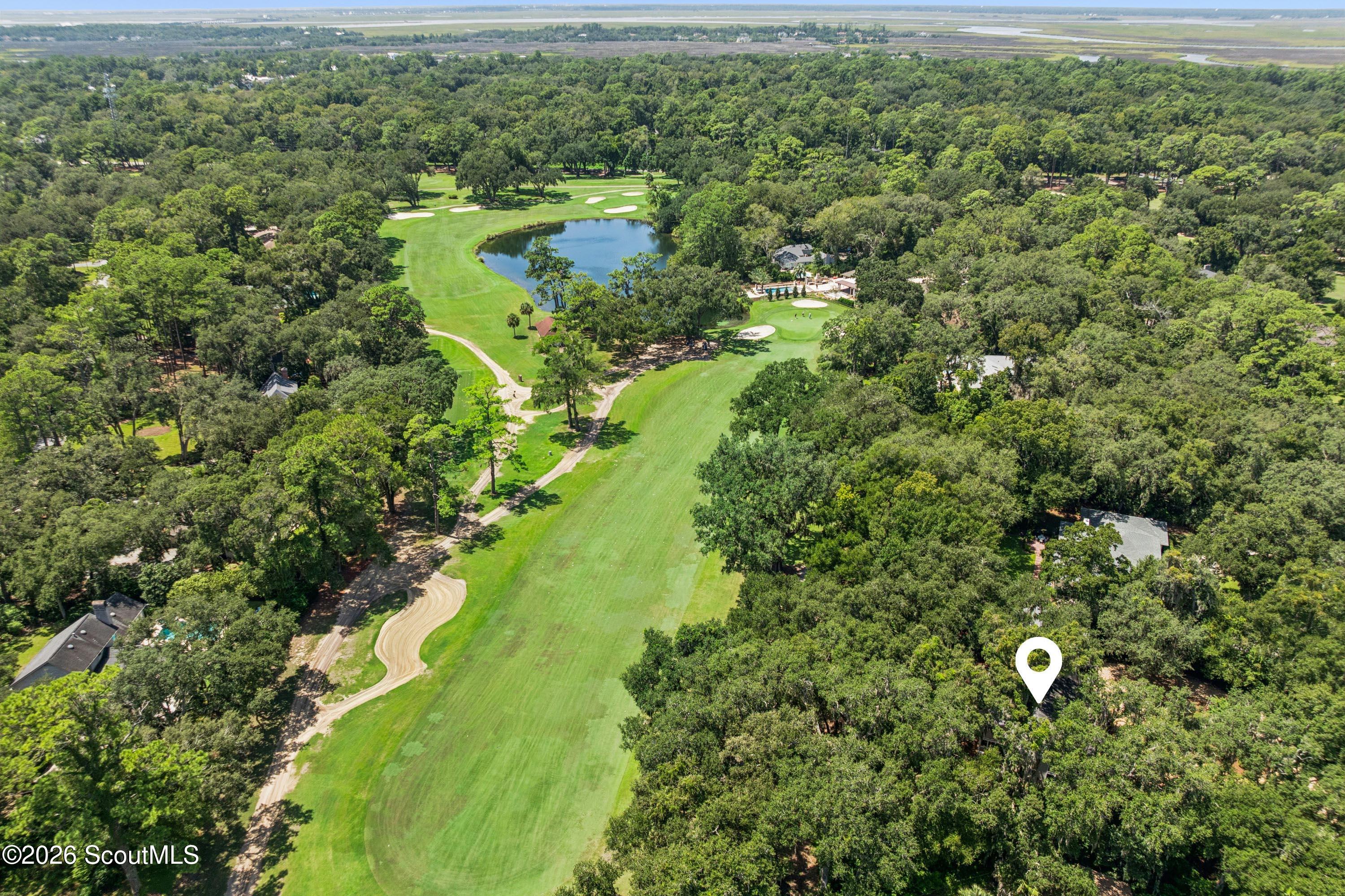 Aerial view of a wooded golf course with a pond and a map pin marking a nearby property.