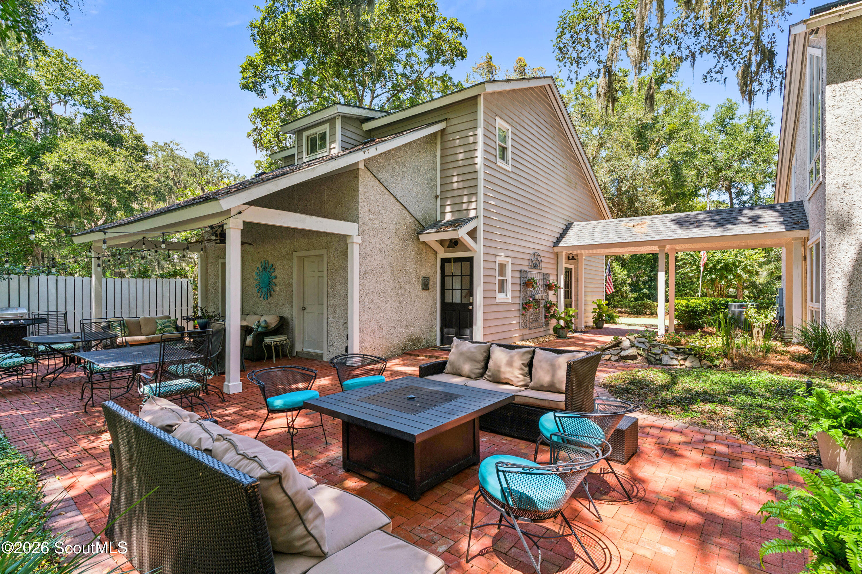 Brick courtyard patio with wicker seating, turquoise chairs, and a covered dining area beside the house.