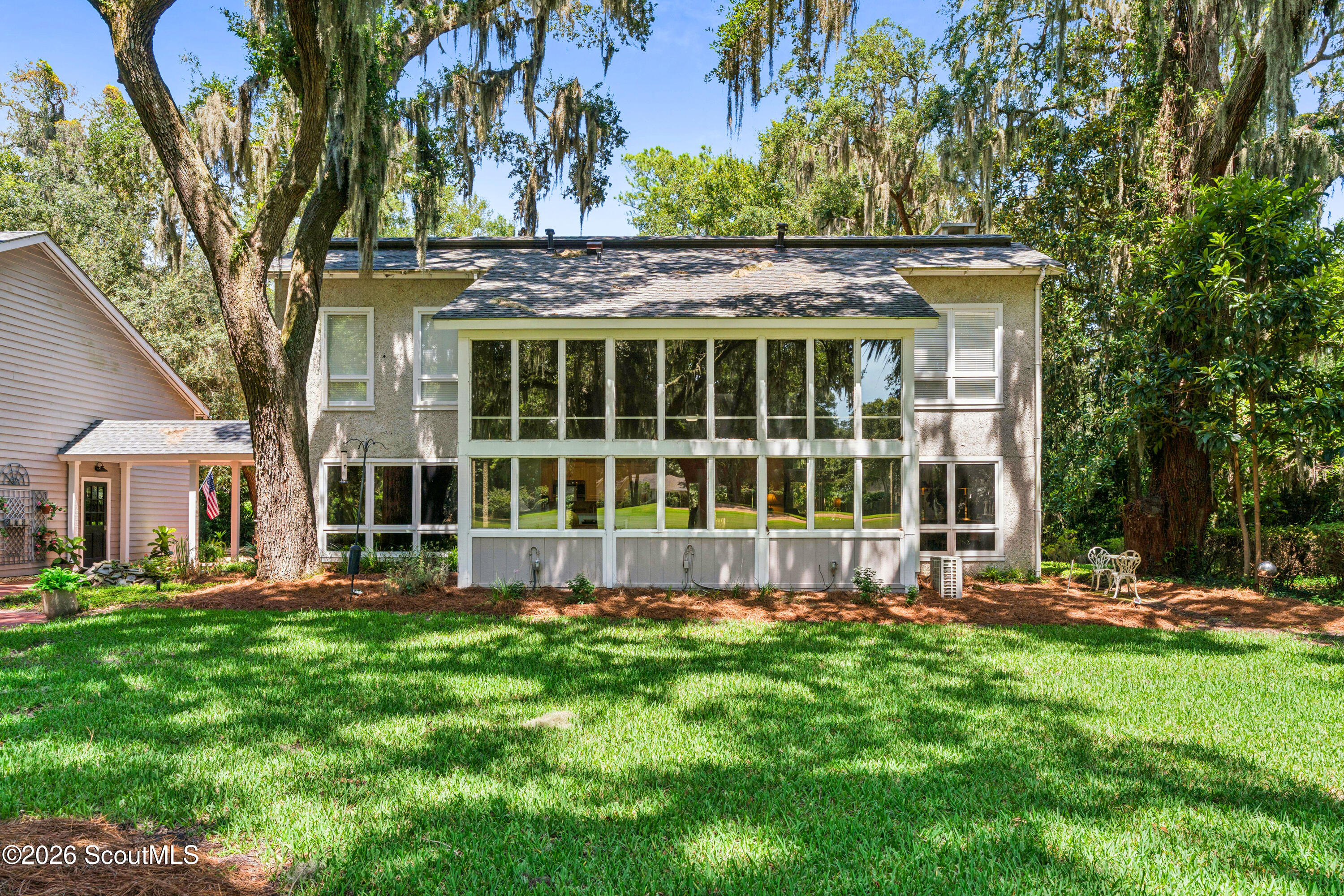 Home’s rear exterior with a large glass-enclosed sunroom beneath moss-draped trees.