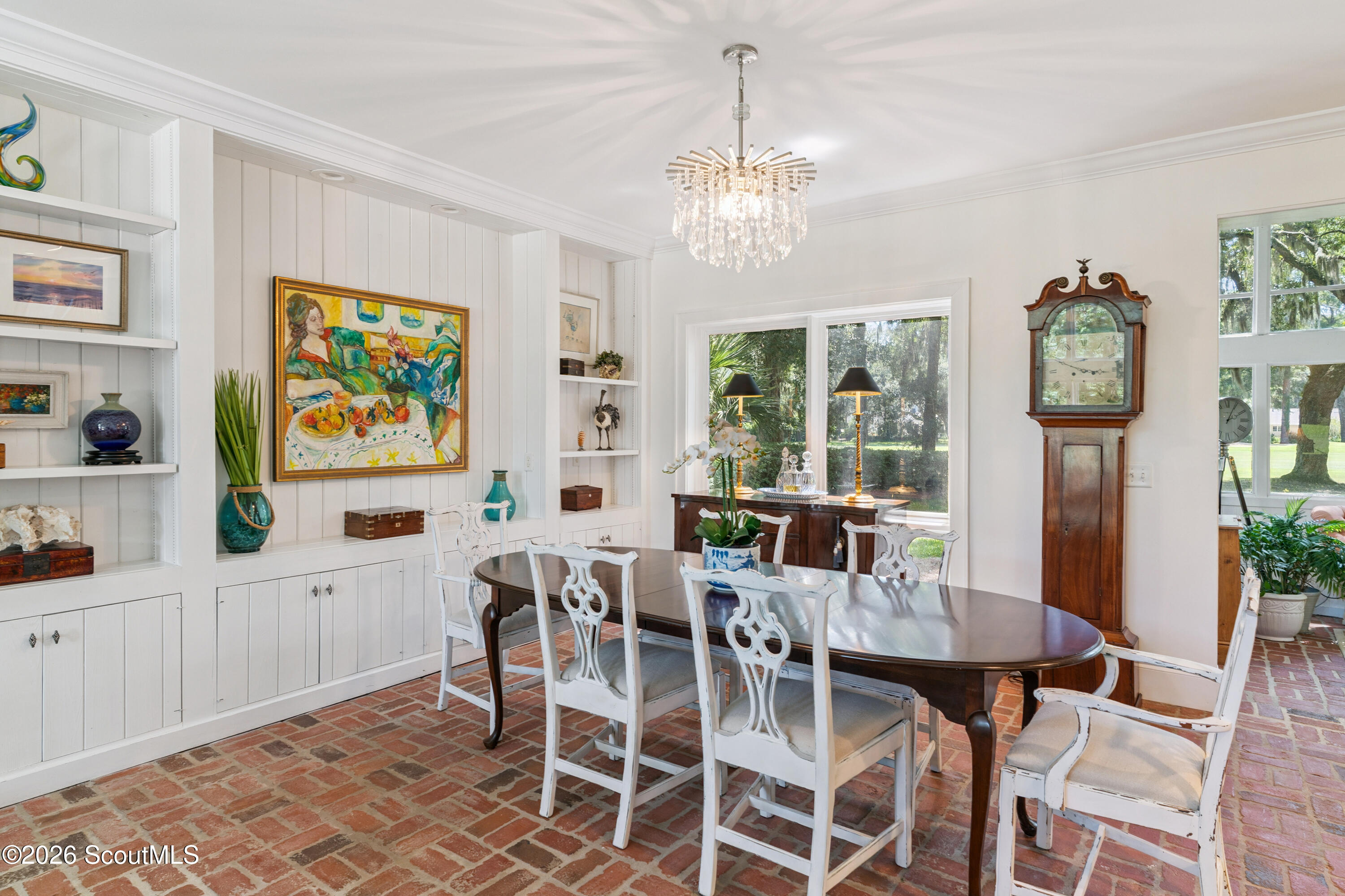 Dining room with brick flooring, built-in display shelves, a crystal chandelier, and a tall grandfather clock.