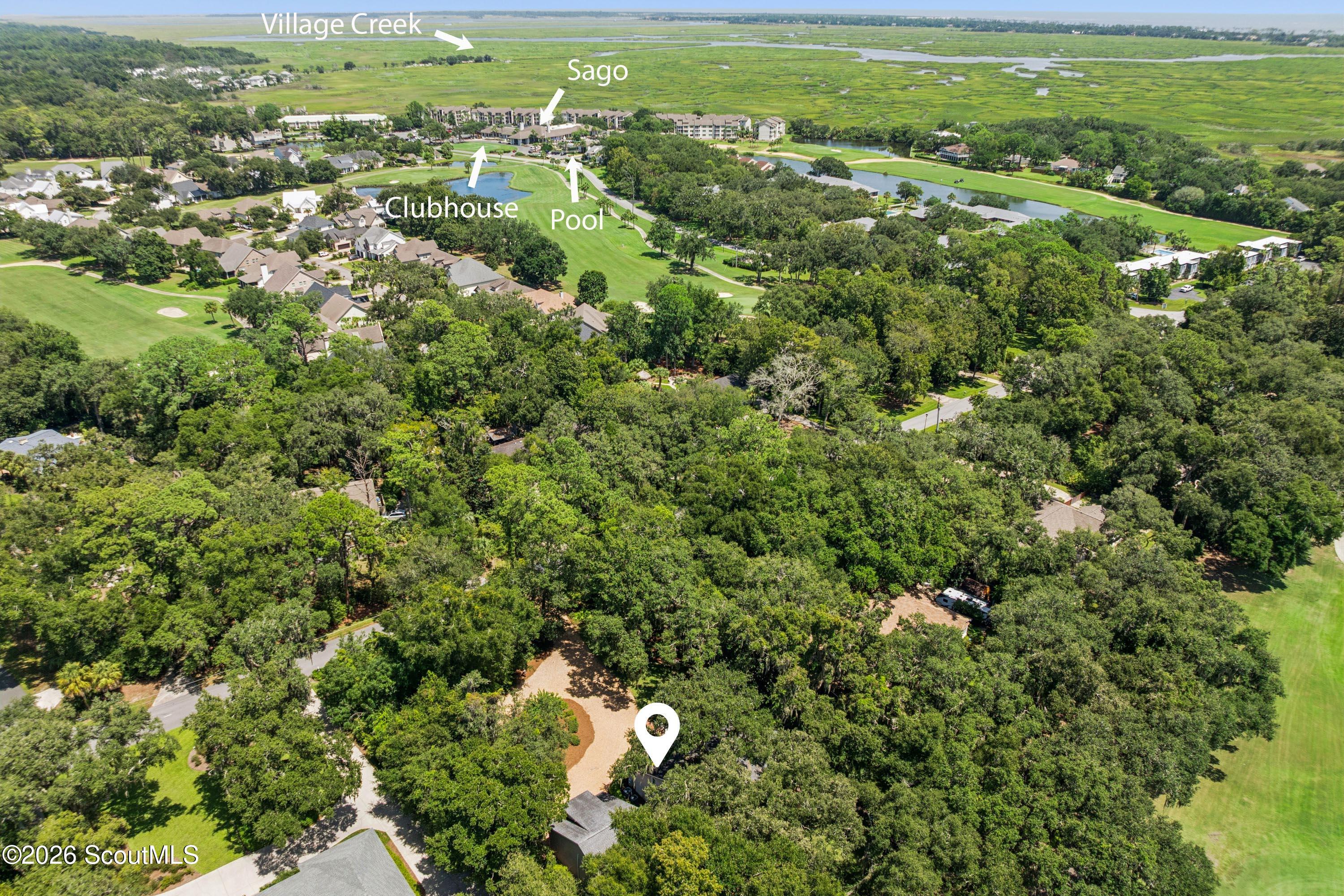 Aerial view of a wooded St. Simons Island property near a golf course, pool, clubhouse, and marshland.
