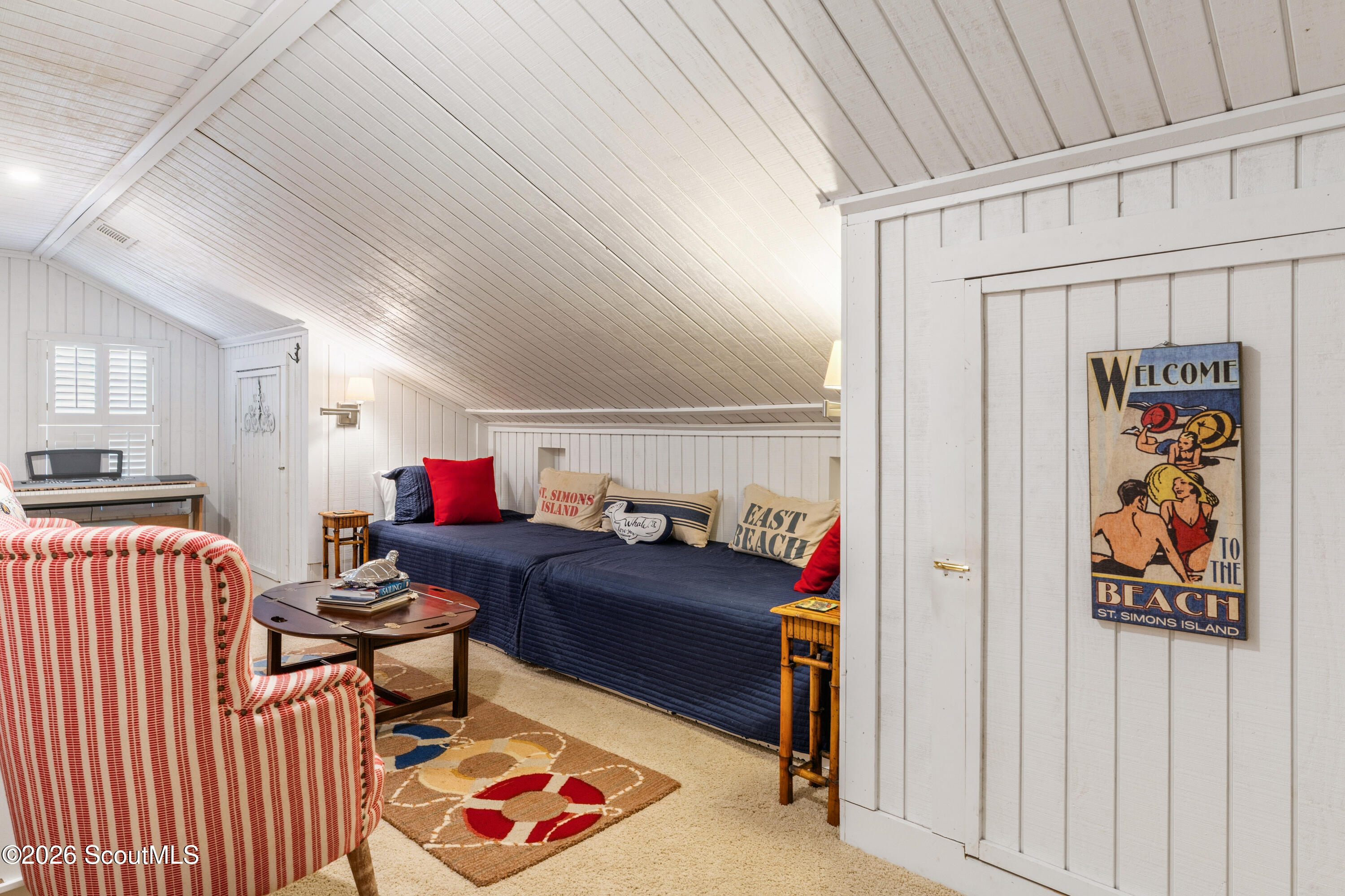 Attic sitting room with a navy daybed, striped armchair, and vintage St. Simons Island beach sign.