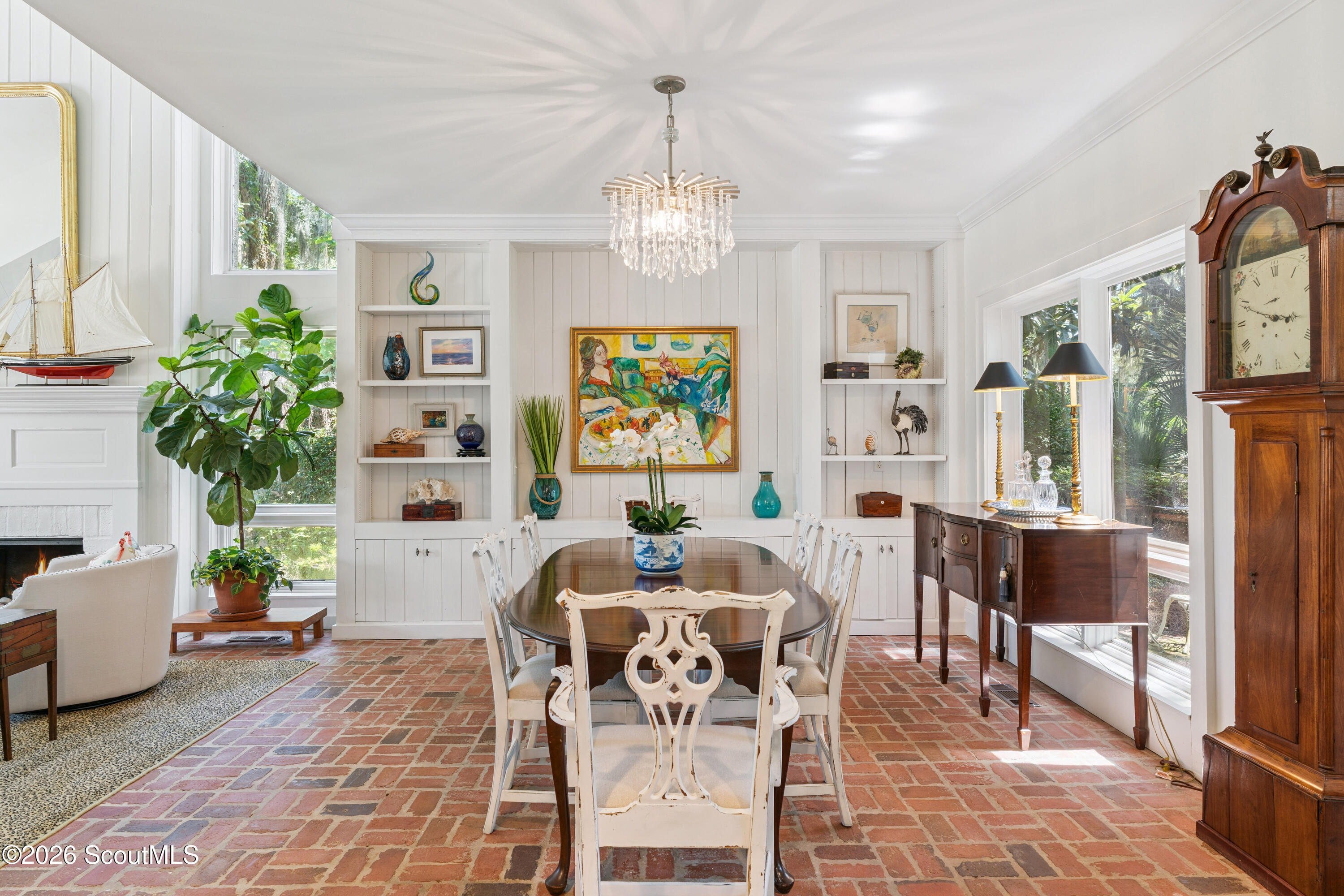 Dining room with brick flooring, built-in shelves, a chandelier, and a long wooden table.
