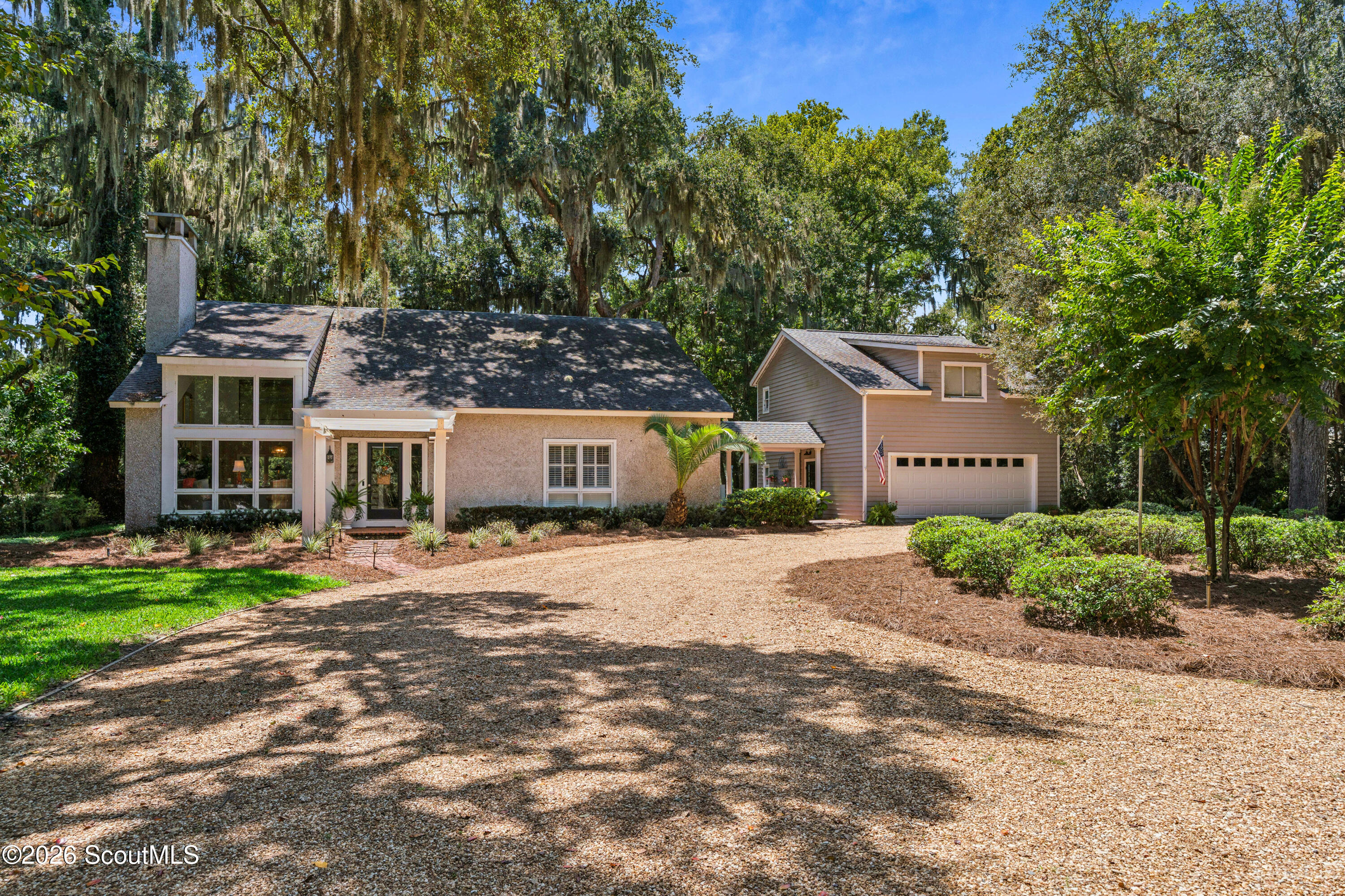 Home with attached garage and gravel driveway beneath mature trees draped in Spanish moss.