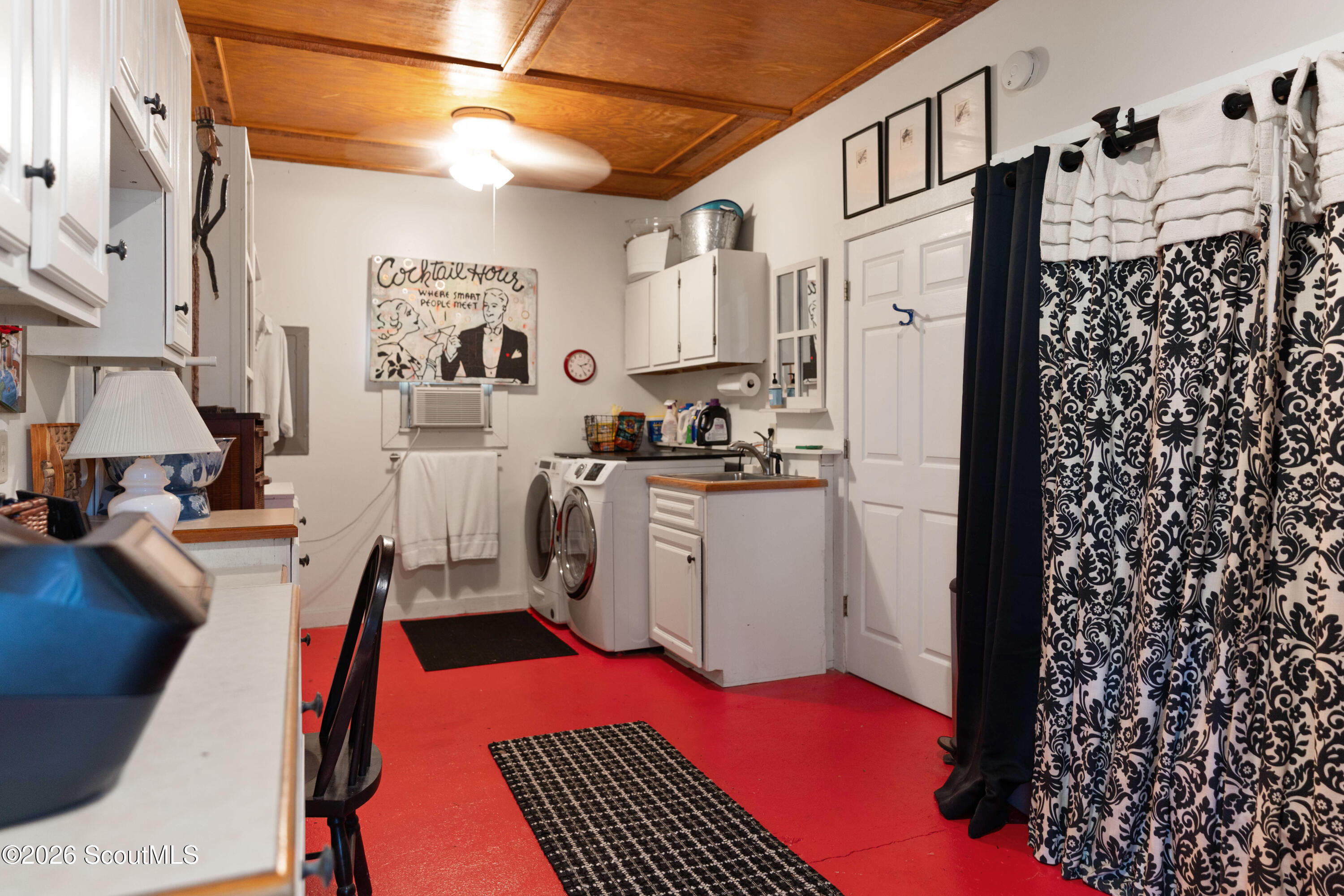 Laundry room with washer and dryer, utility sink, vivid red floor, and wood-paneled ceiling.