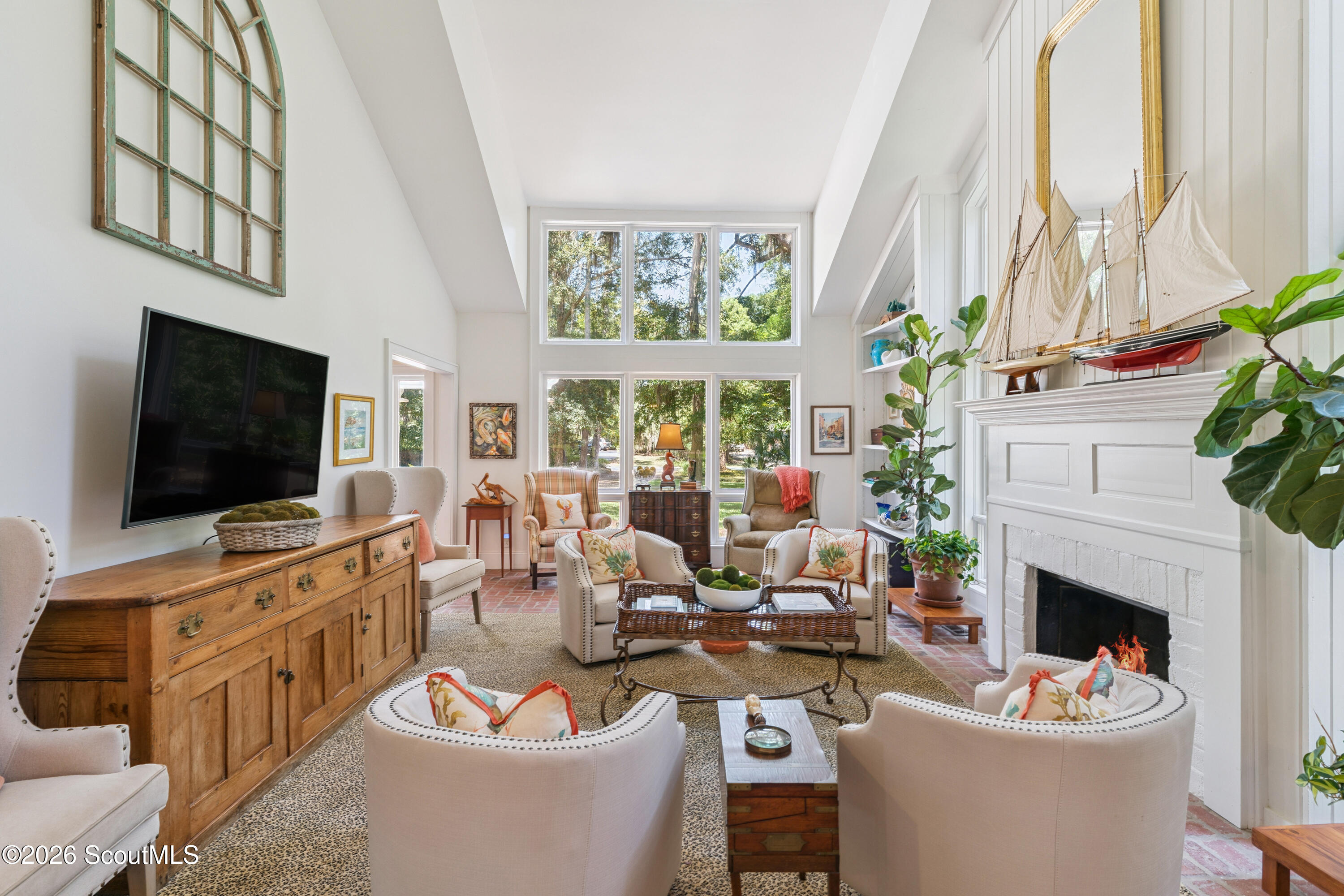 Bright living room with tall windows, a white fireplace, model sailboat, and upholstered seating.