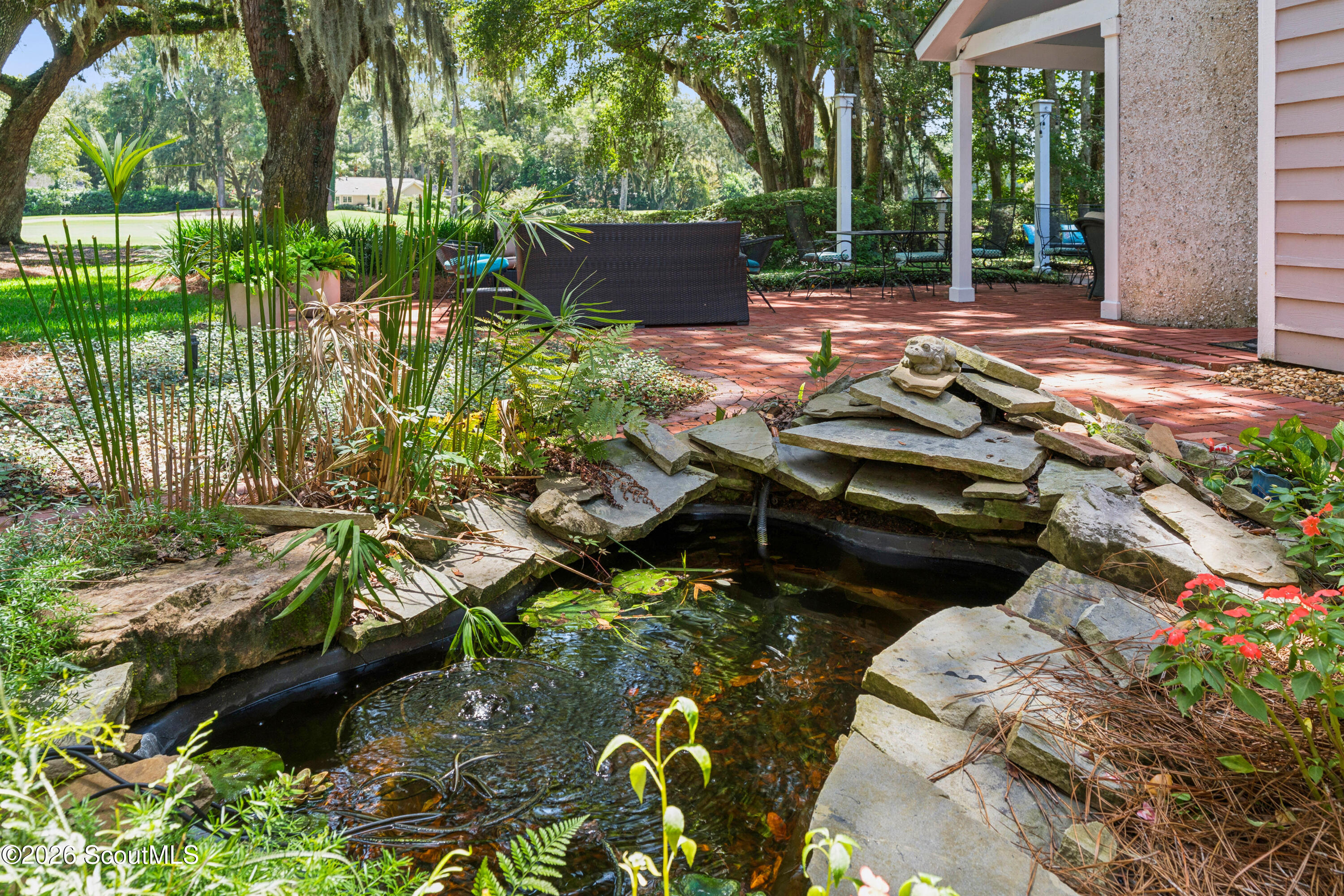 Backyard patio with a stone-edged pond, brick terrace, and shaded outdoor seating.
