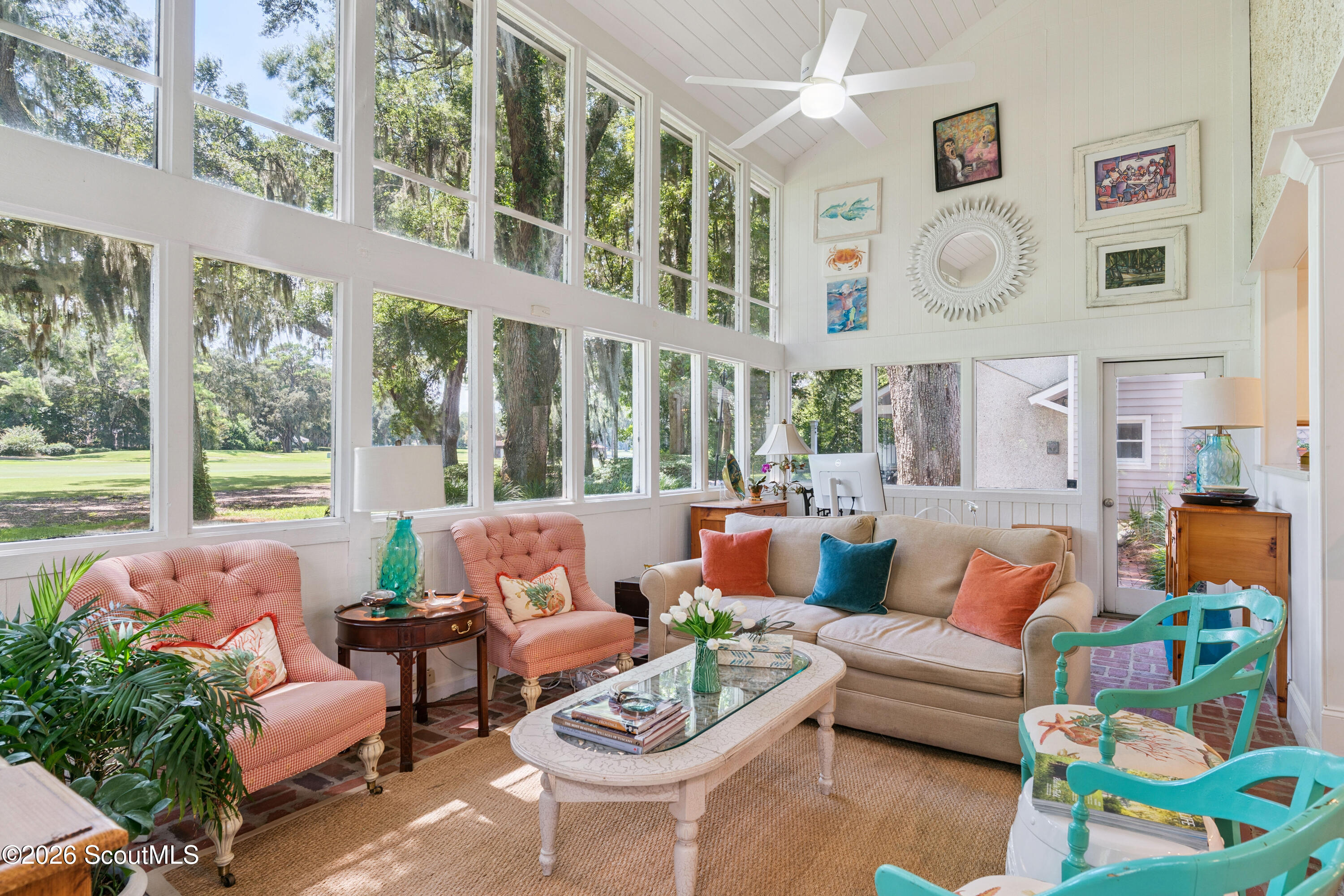Sunroom with tall windows, a vaulted ceiling, patterned armchairs, and a beige sofa.