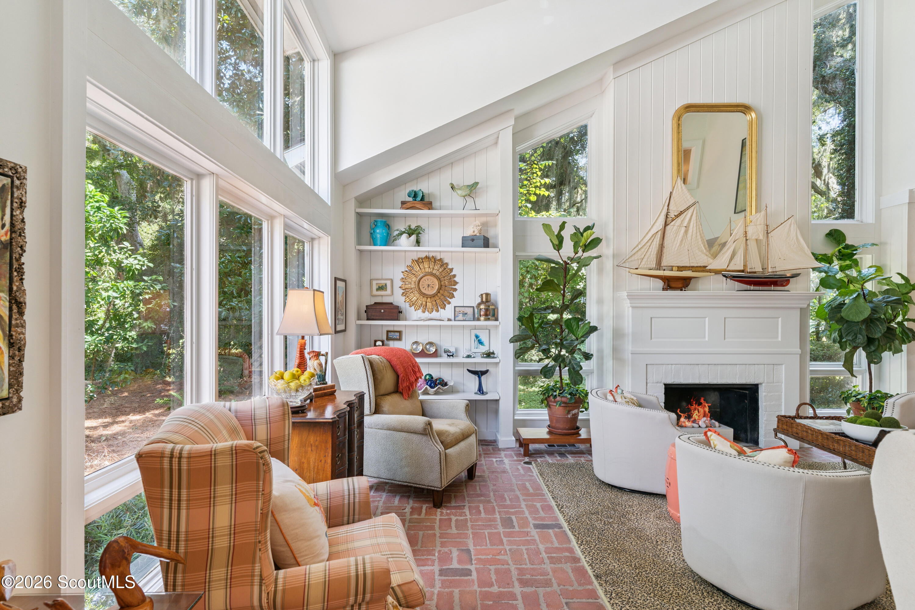 Bright living room with tall windows, brick flooring, and a white fireplace topped with model sailboats.