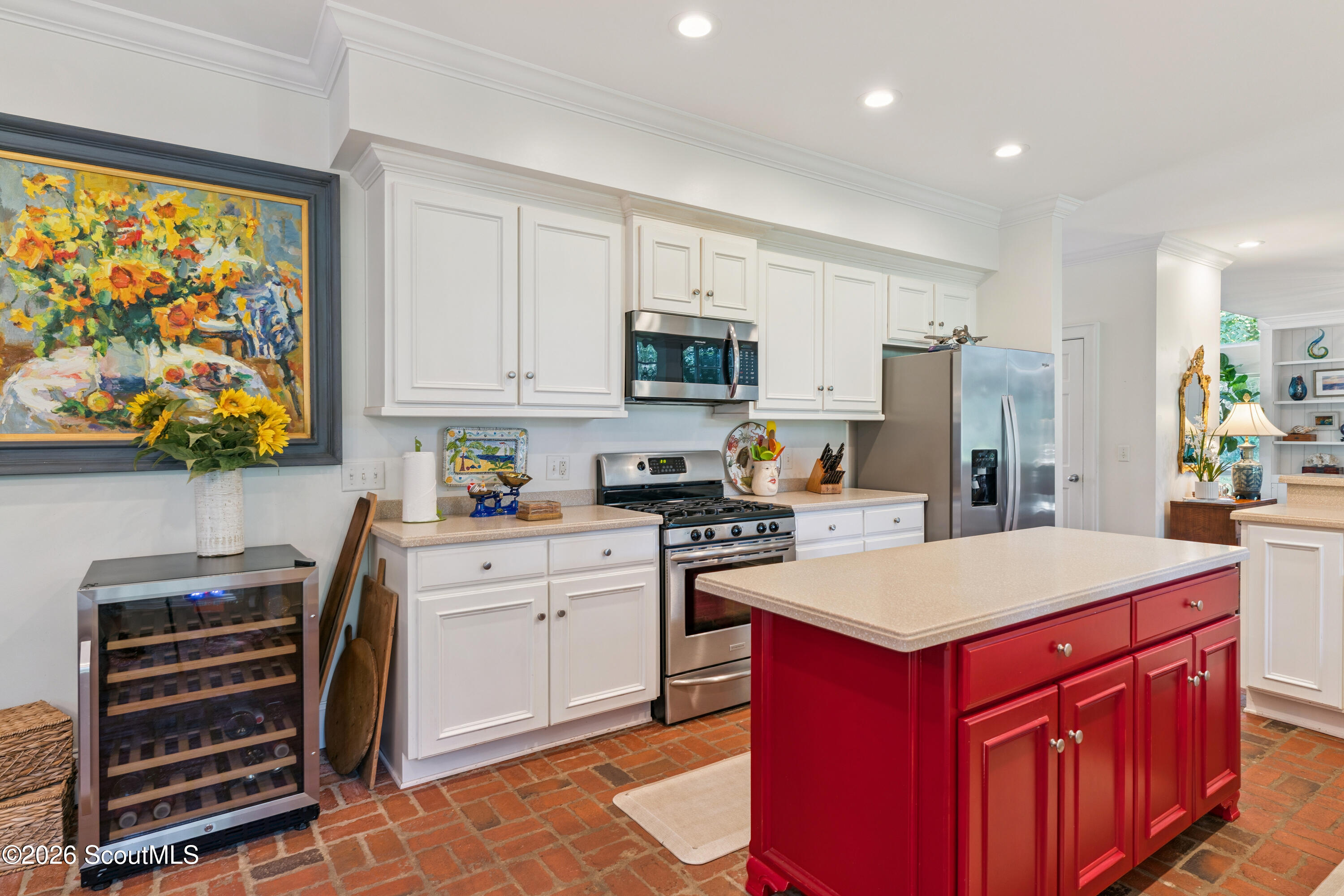 Kitchen with a red island, white cabinets, stainless steel appliances, and brick flooring.