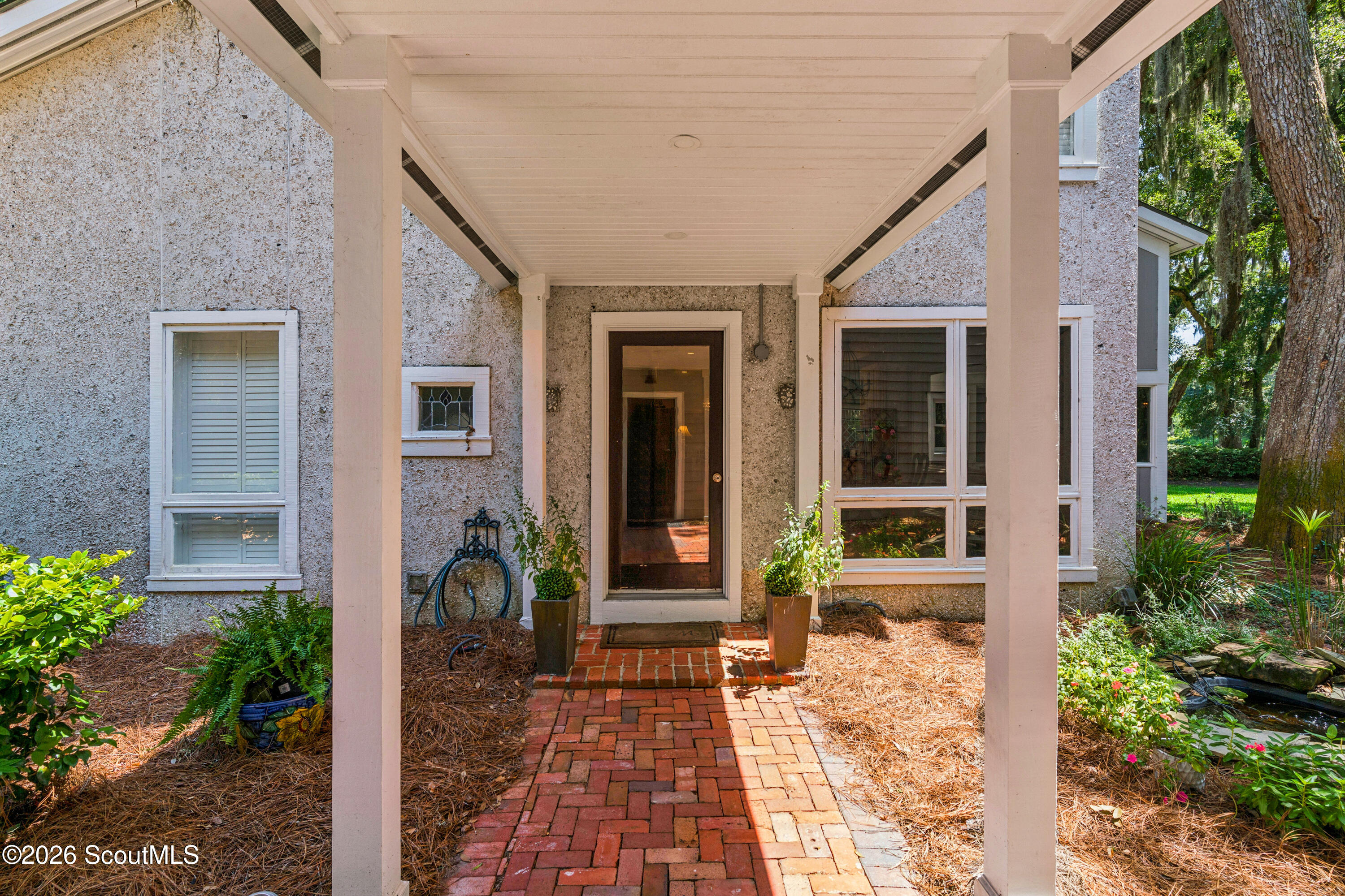 Home entrance with a covered porch, brick walkway, white columns, and landscaped garden beds.