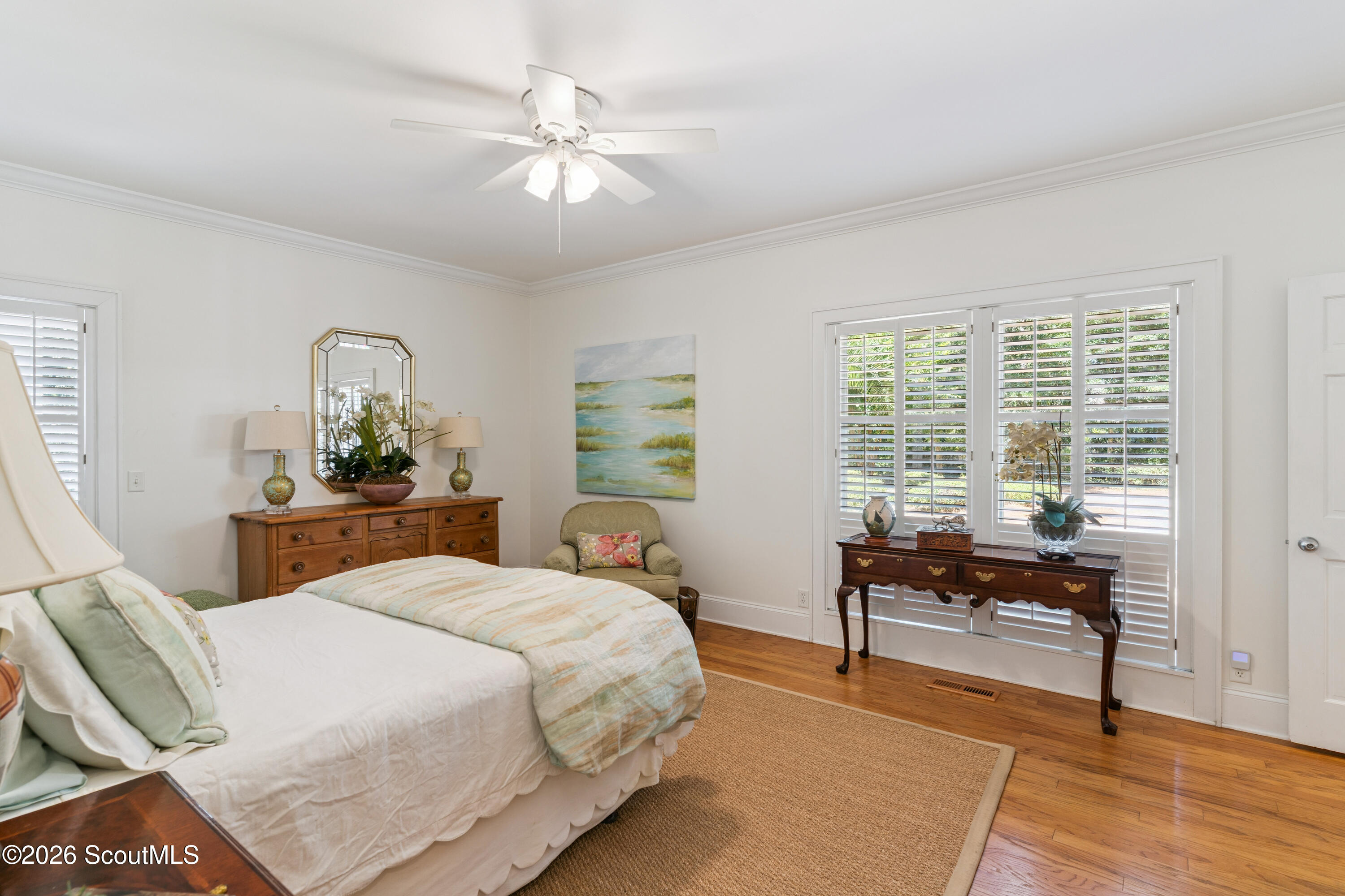 Furnished bedroom with pale green bedding, wood furniture, and plantation-shuttered windows.