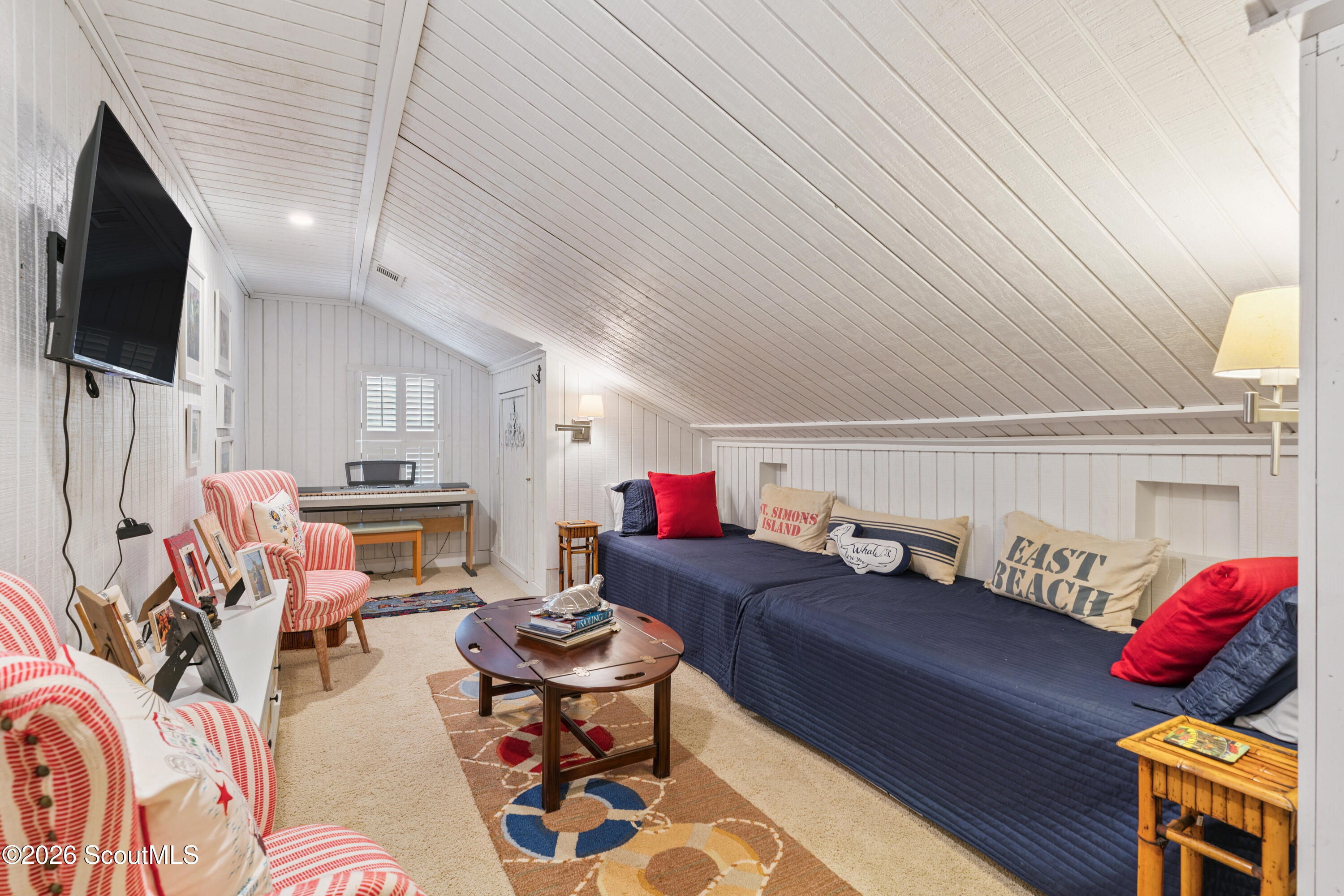 Furnished attic sitting room with a navy daybed, striped armchairs, and a sloped white plank ceiling.