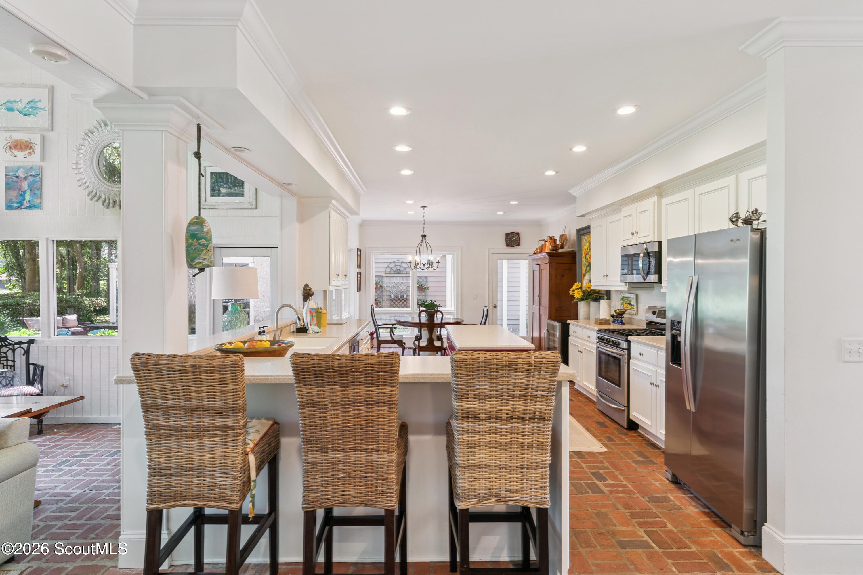 Bright kitchen with white cabinets, stainless appliances, a large island, and woven bar stools.
