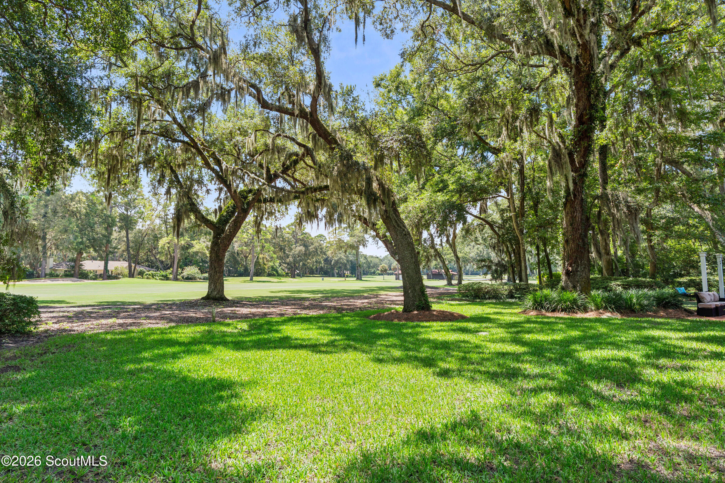 Manicured golf course lawn framed by sprawling live oaks draped with Spanish moss.