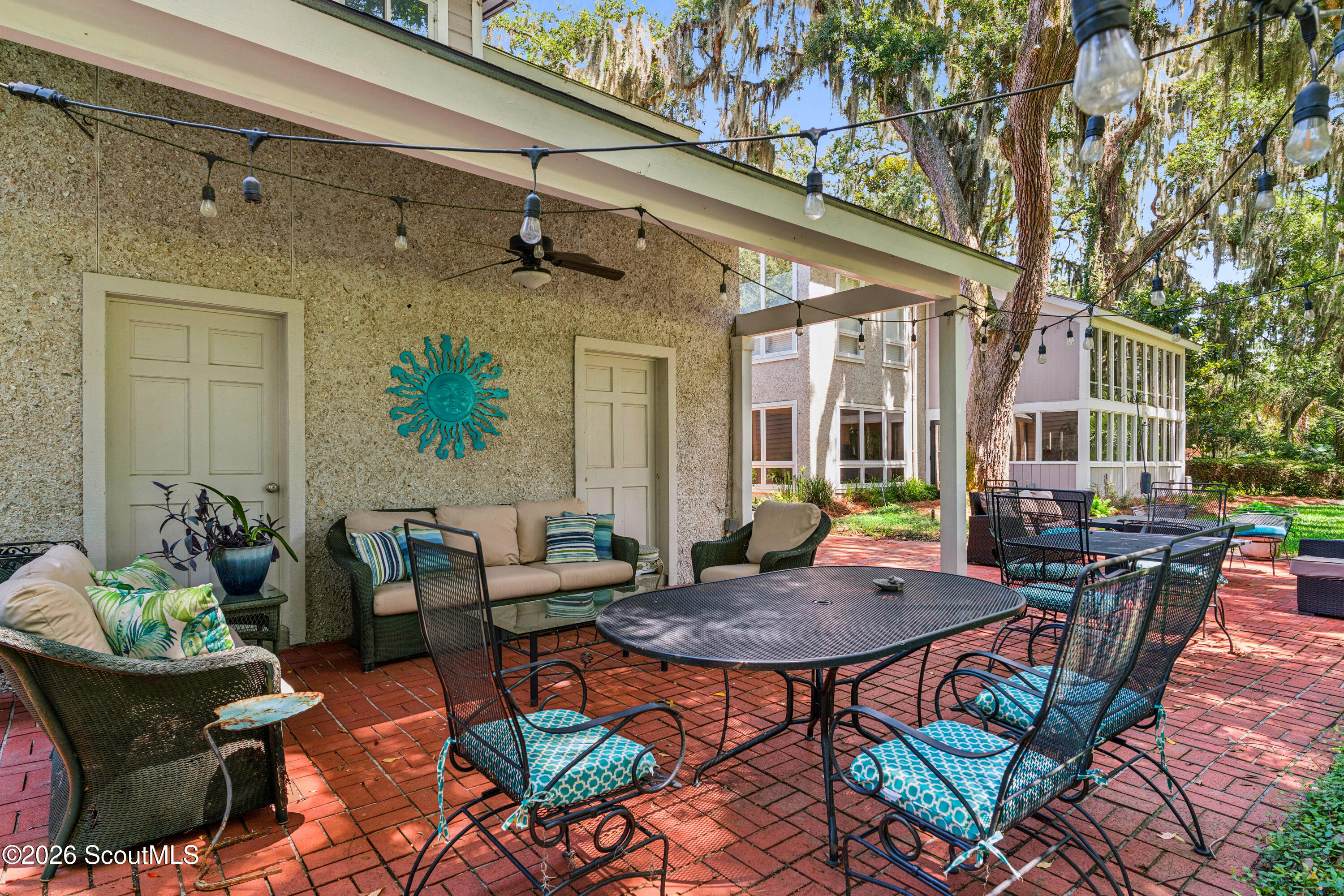 Covered brick patio with wrought-iron dining set, string lights, and outdoor lounge seating.