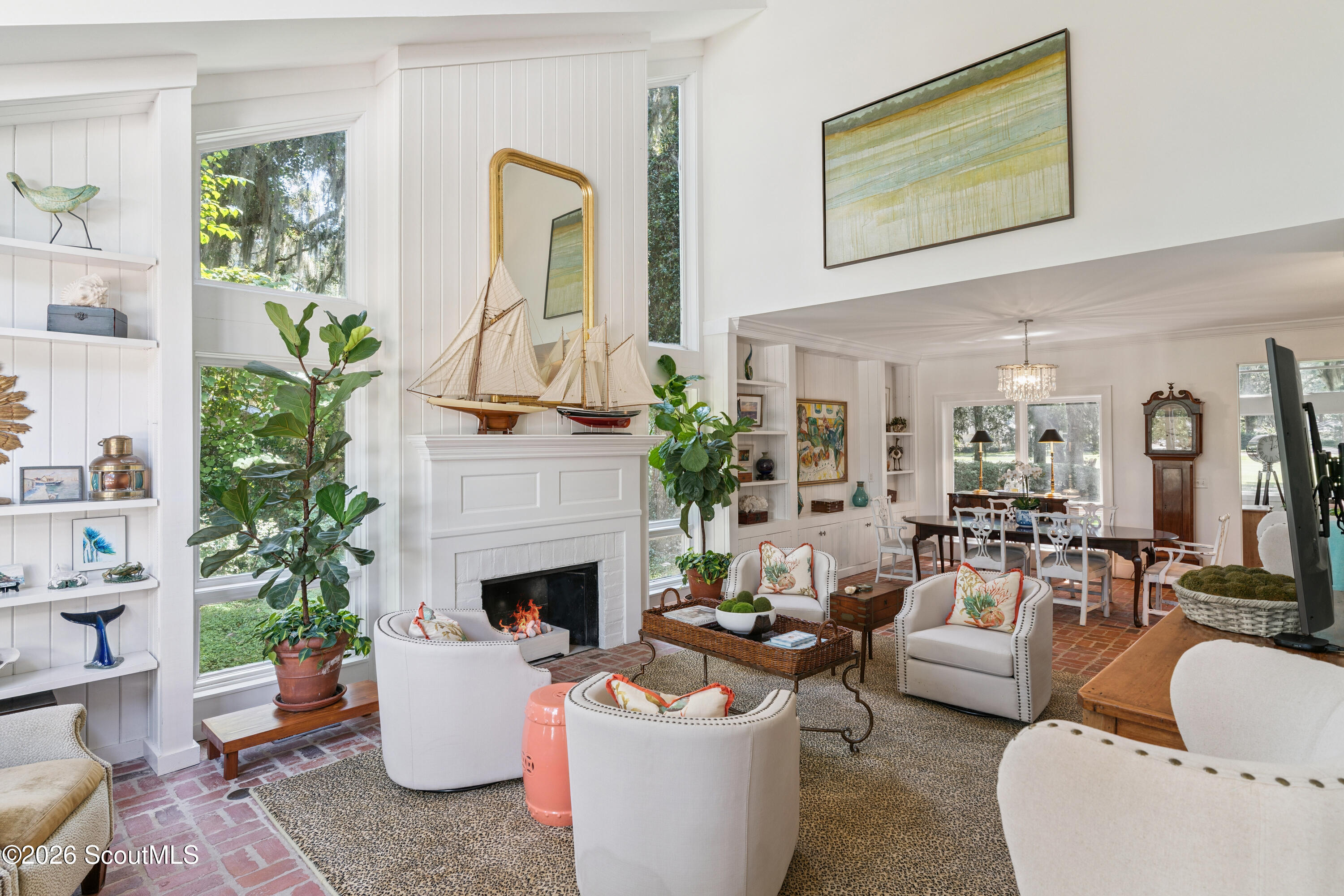Bright living room with a white fireplace topped by model sailboats and an adjoining dining area.