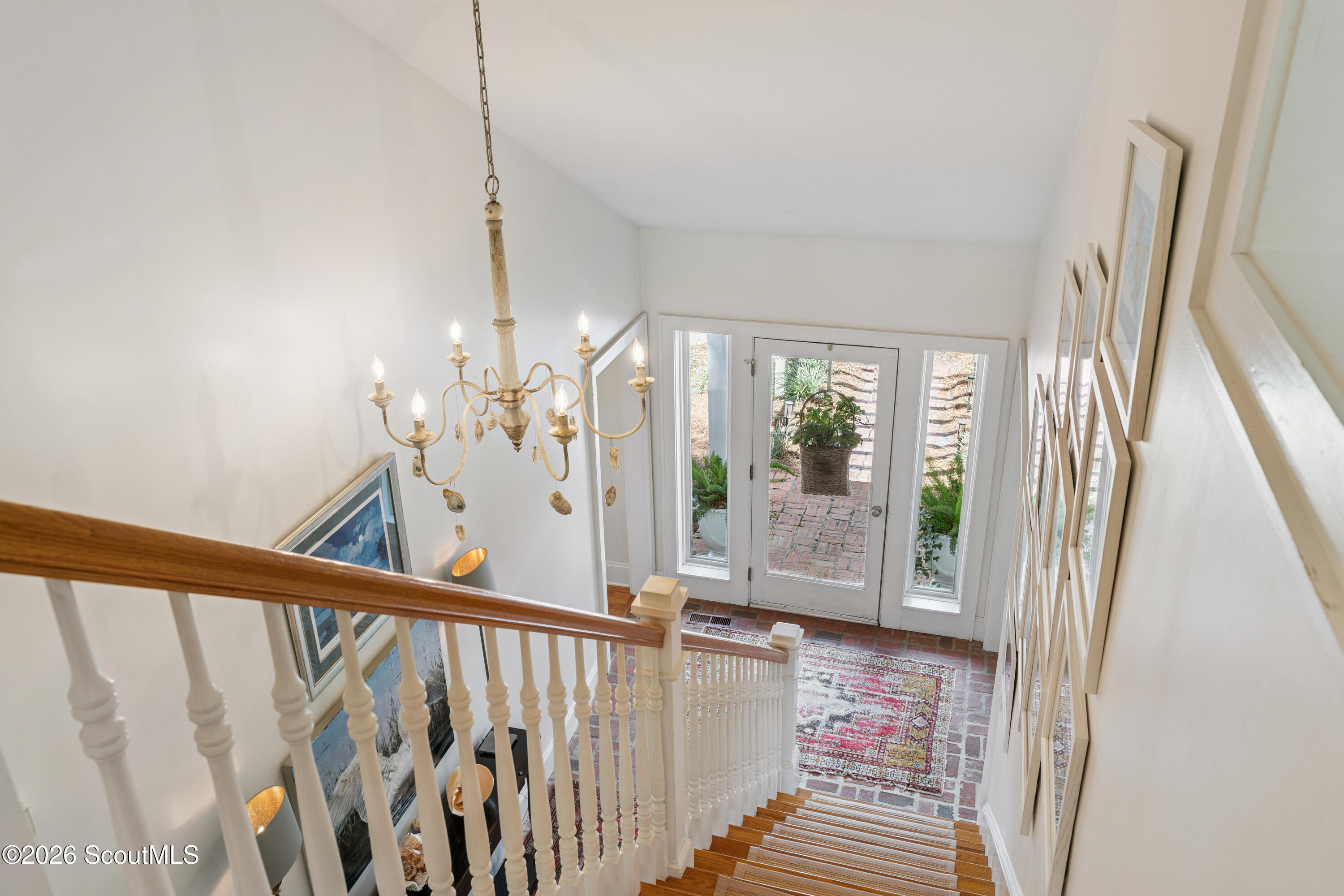 Entry foyer with a descending staircase, rustic chandelier, and glass-paneled front door.