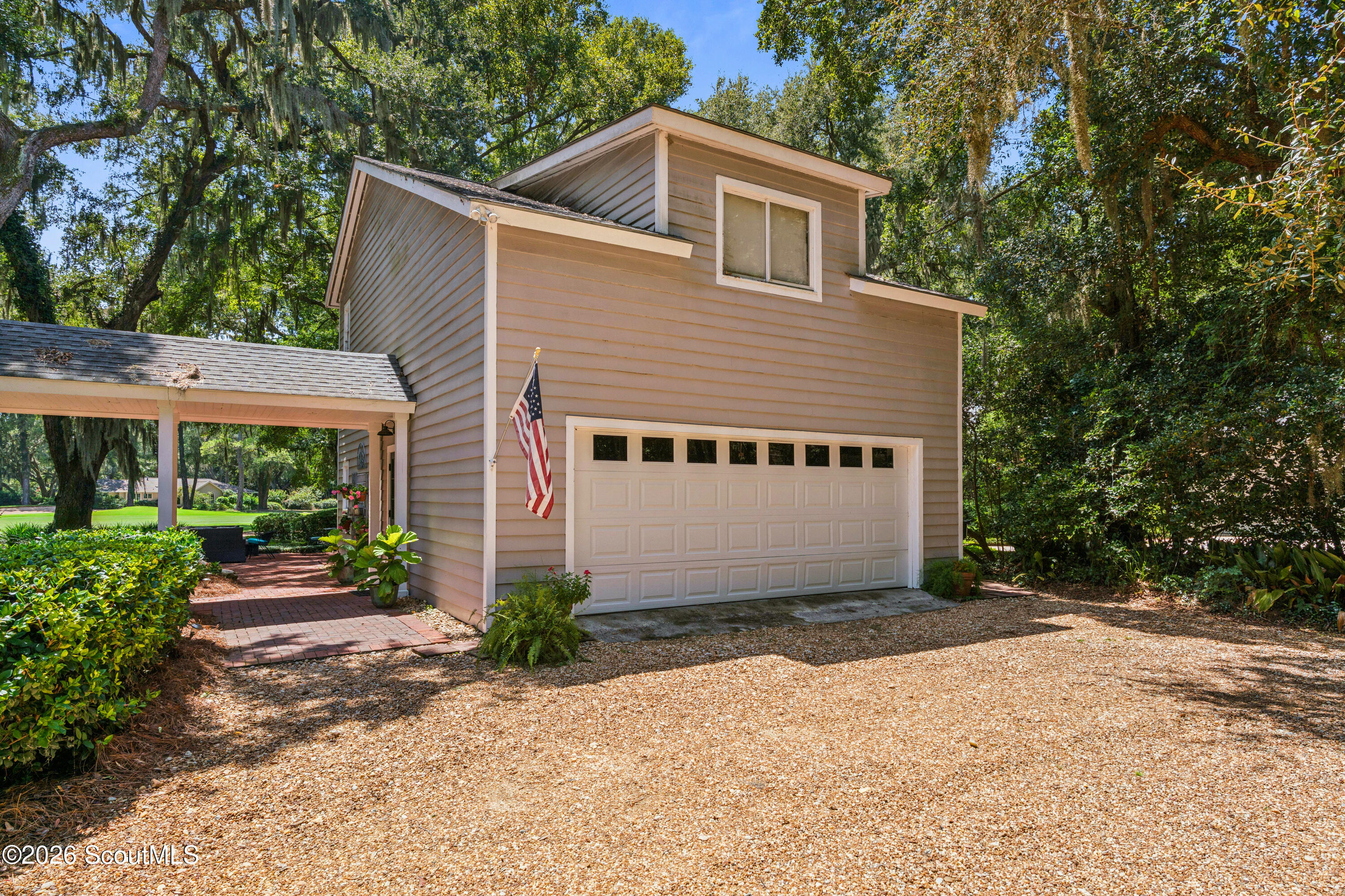 Two-story home with an attached double garage and covered carport beneath mature trees.