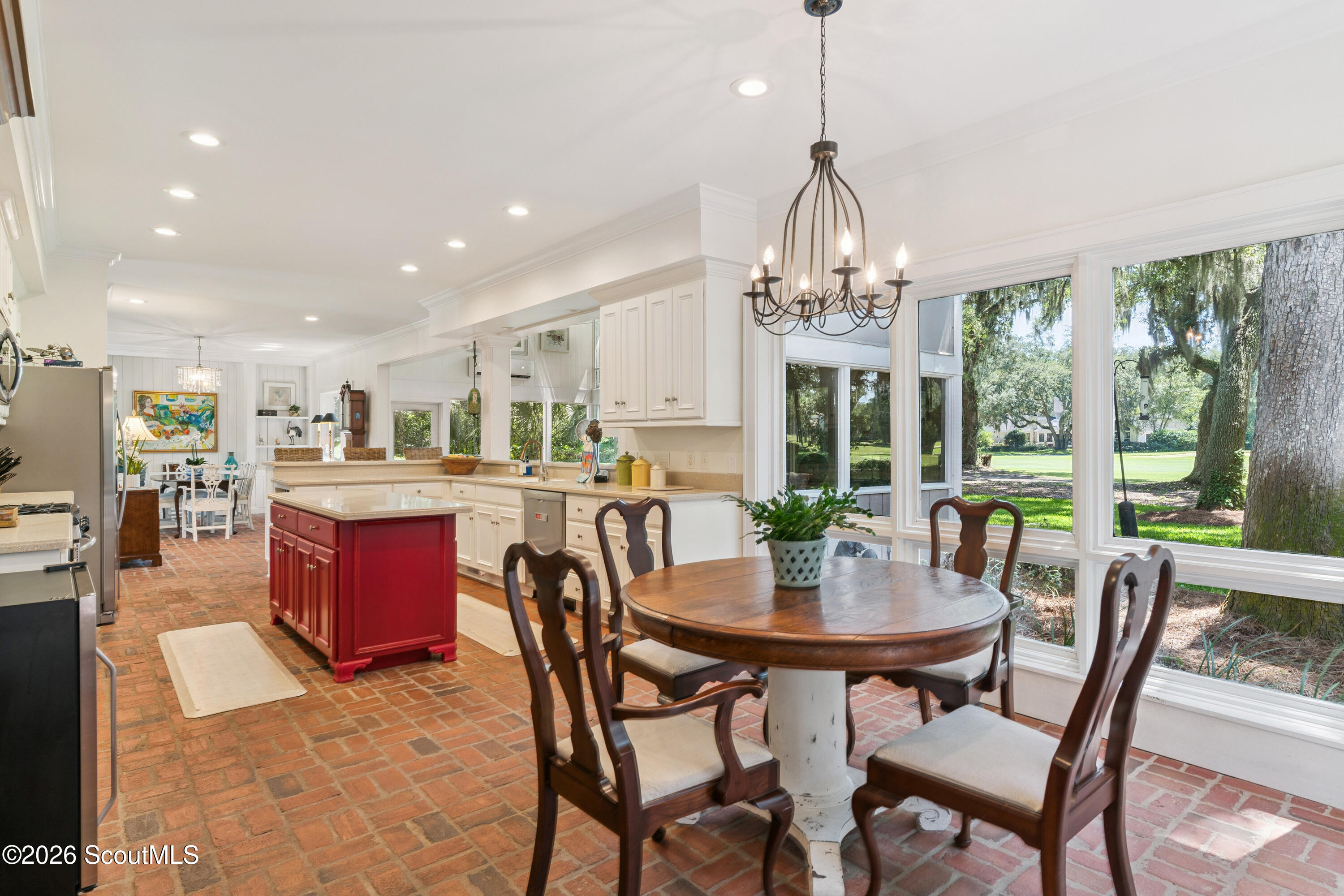 Kitchen and dining area with a red island, brick floors, and large windows overlooking trees.