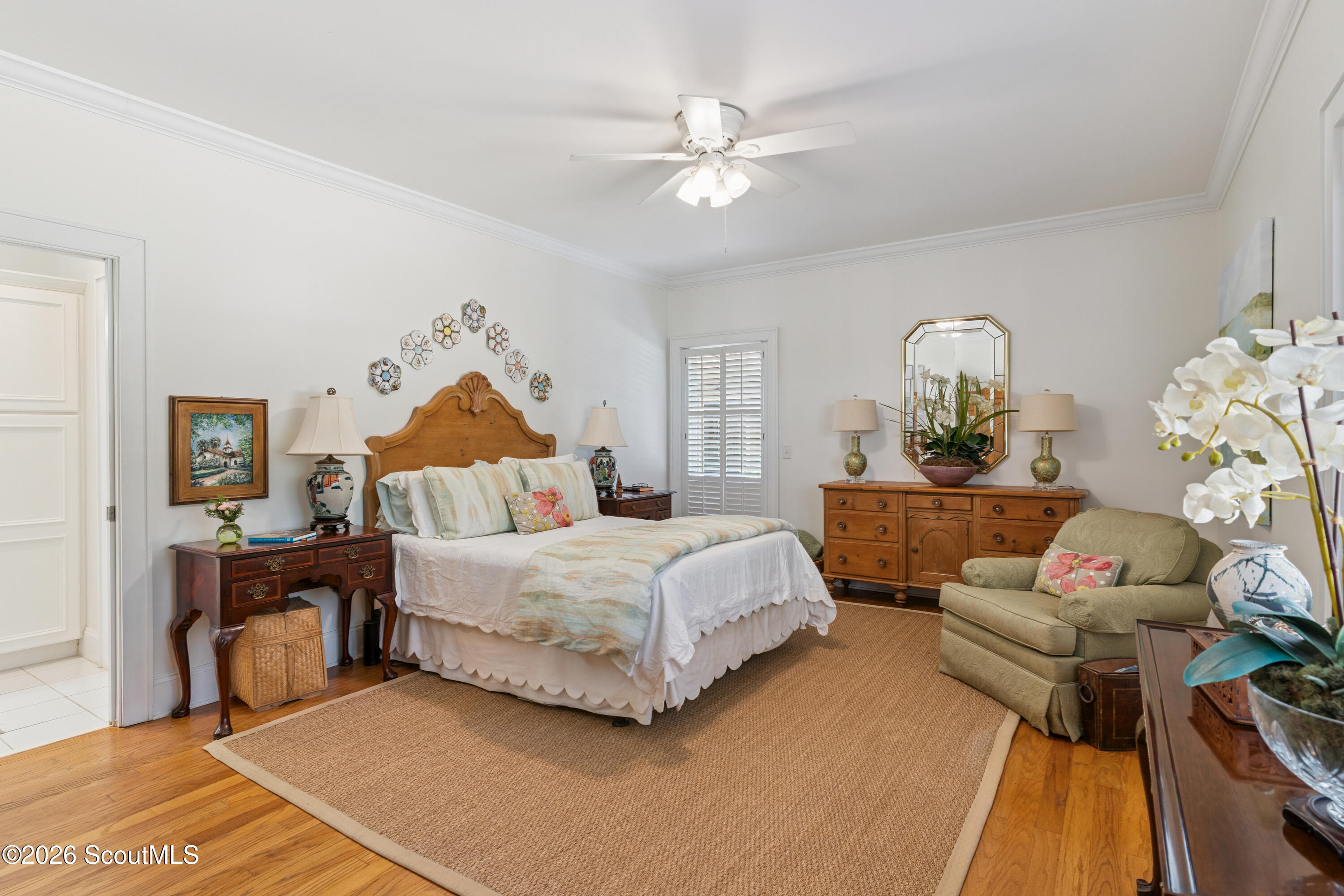 Furnished bedroom with a carved wooden bed, matching dresser, shuttered window, and woven rug.