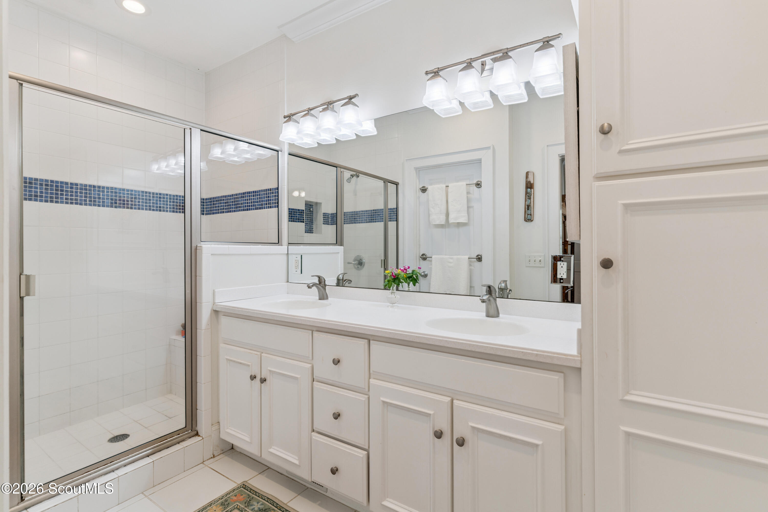 Bathroom with a glass shower, blue tile accent stripe, and long double-sink vanity.