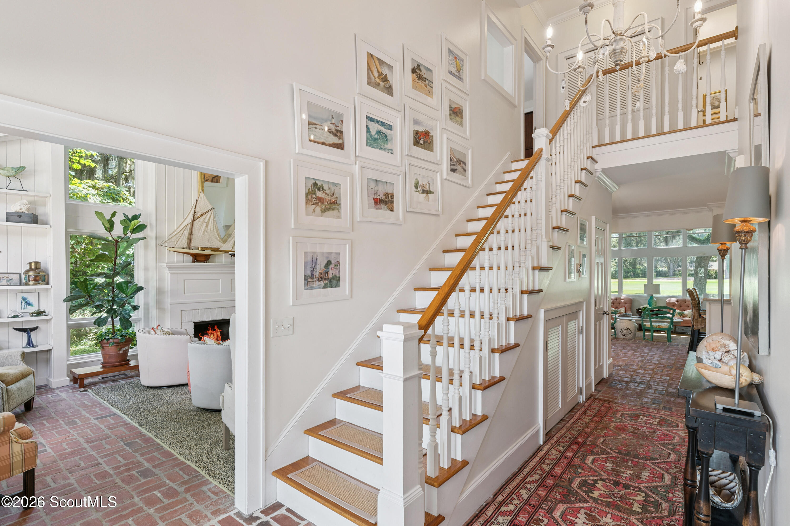 Bright foyer with a wood-railed staircase, gallery wall, brick floors, and adjoining sitting room.
