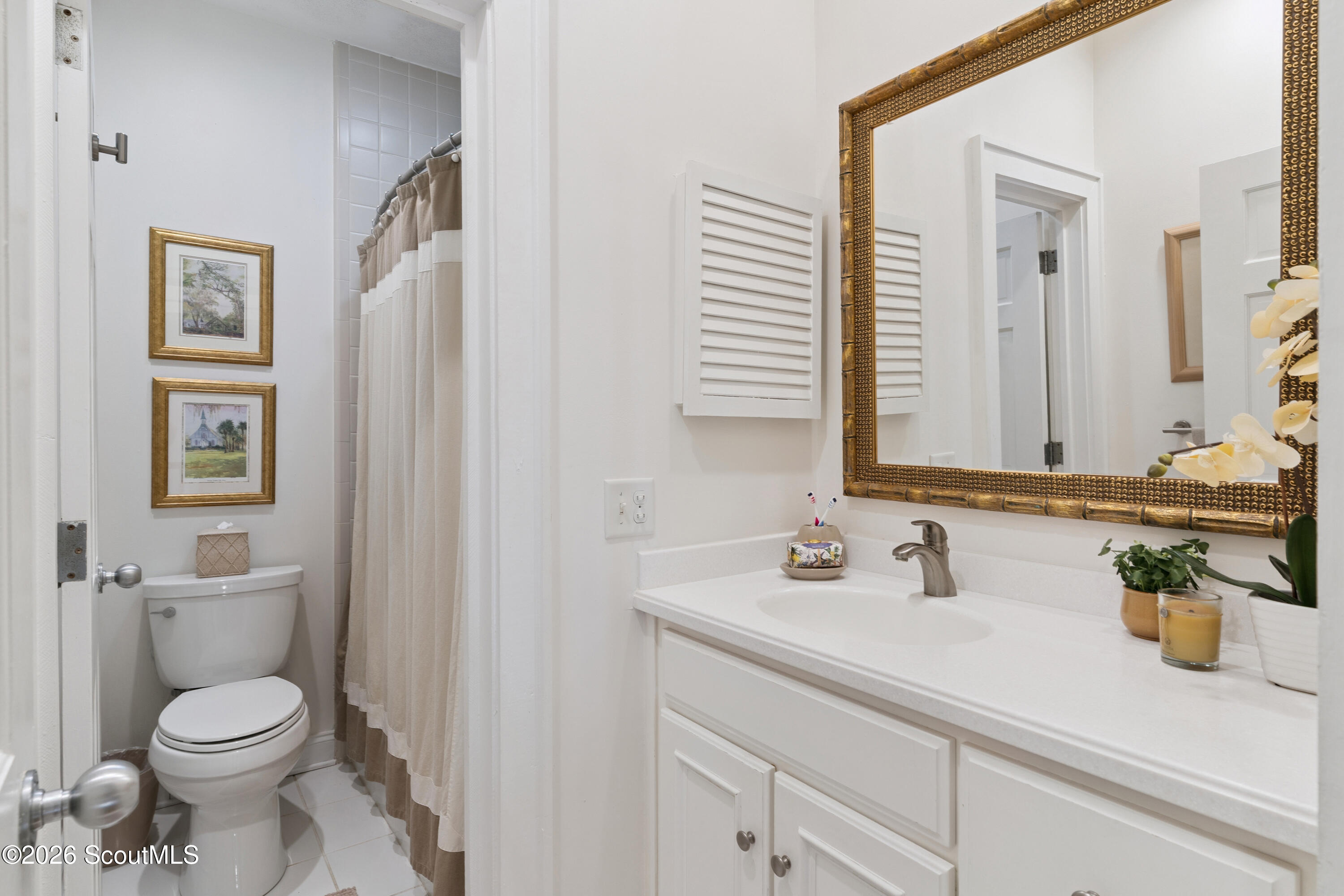 Bathroom with white vanity, ornate gold-framed mirror, toilet, and beige shower curtain.