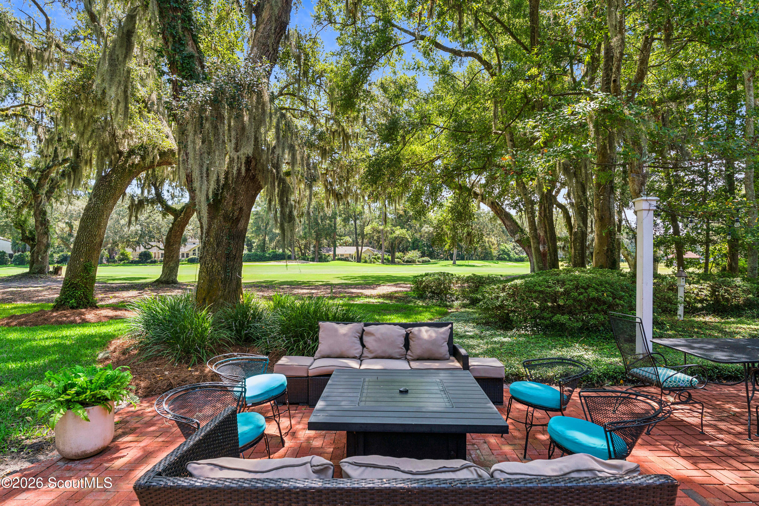 Furnished brick patio beneath moss-draped oaks, overlooking a broad green lawn.