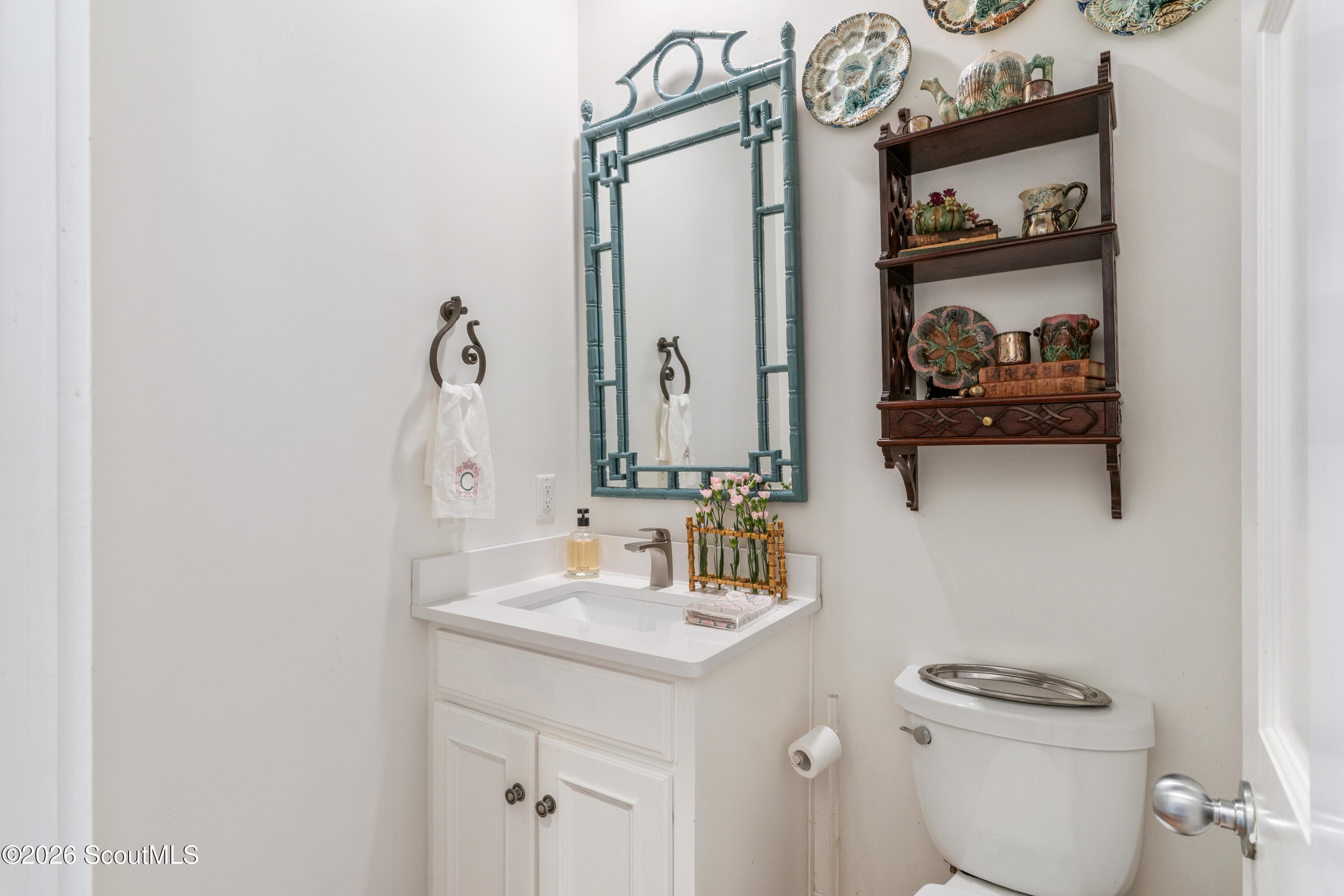 Bathroom with a white vanity, blue-green framed mirror, and decorative pottery on wall shelves.