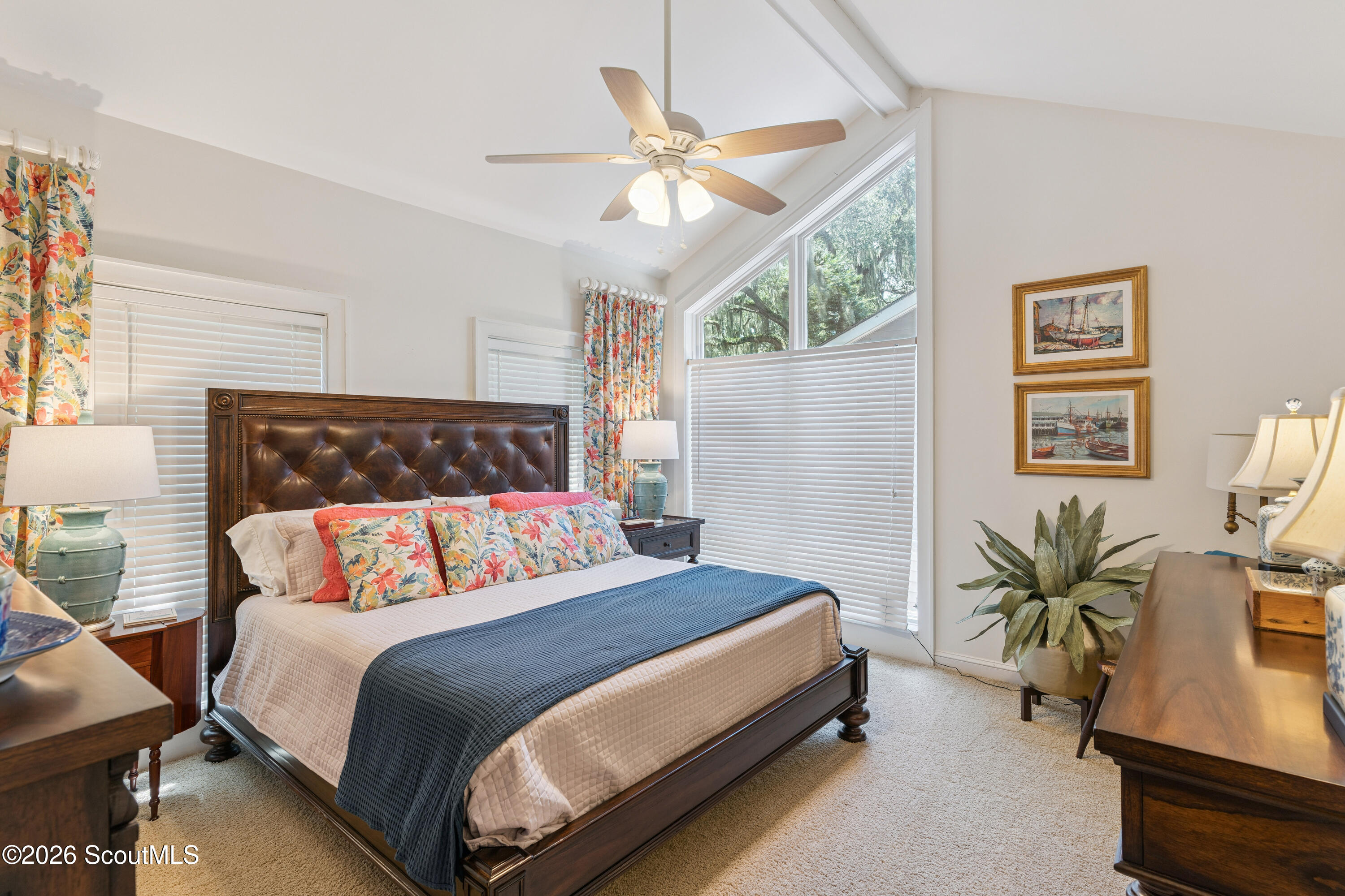 Bedroom with a dark wood bed, floral pillows, and tall windows with blinds.