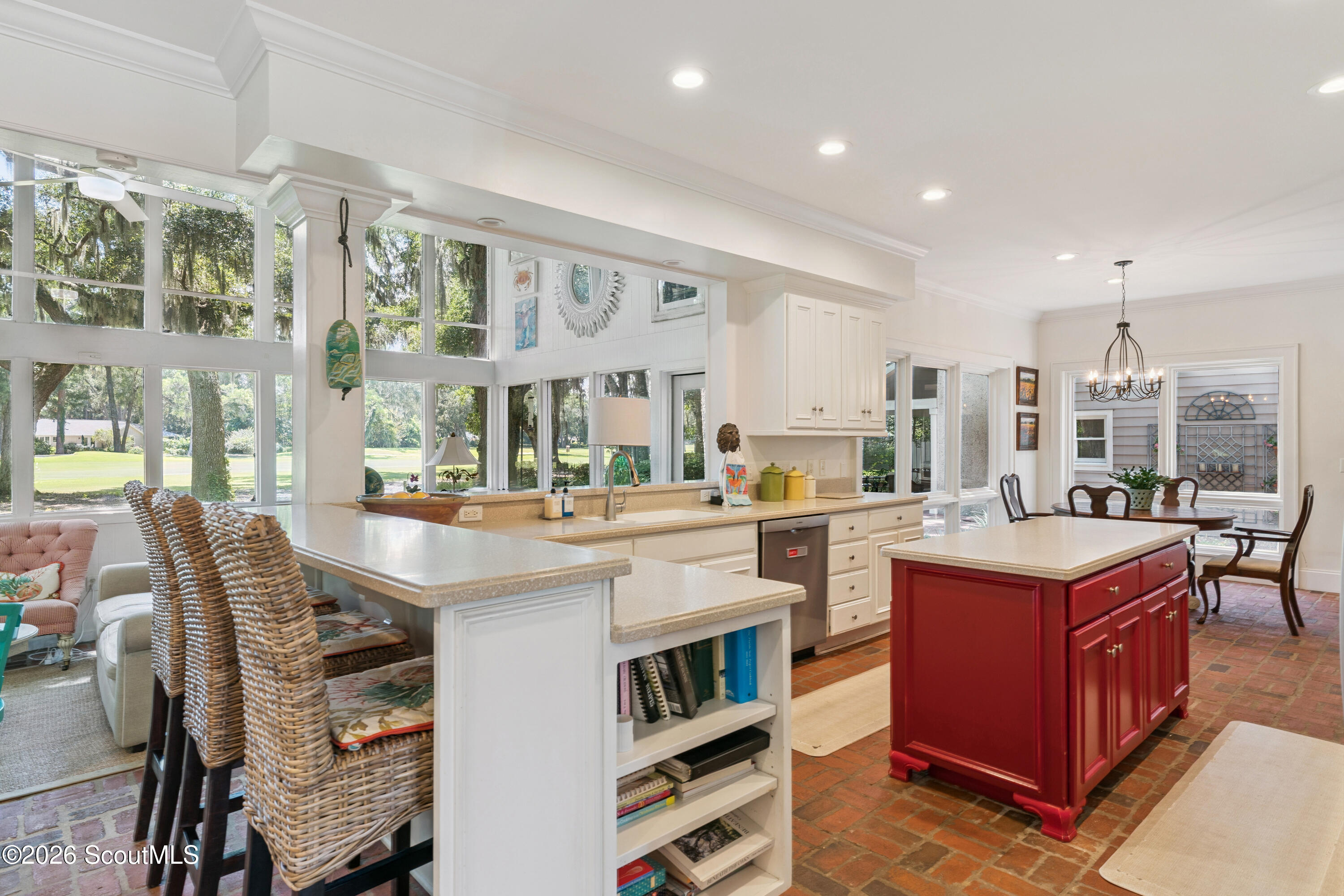 Bright kitchen with a red island, brick floors, and large windows overlooking trees.