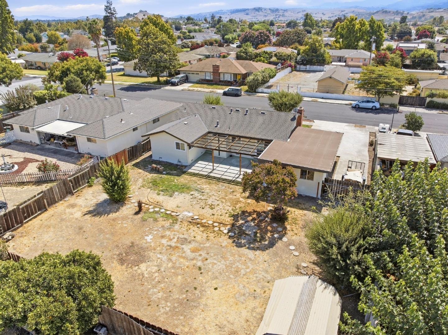 Aerial view of a home with a large dry backyard, covered pergola, and distant hills.