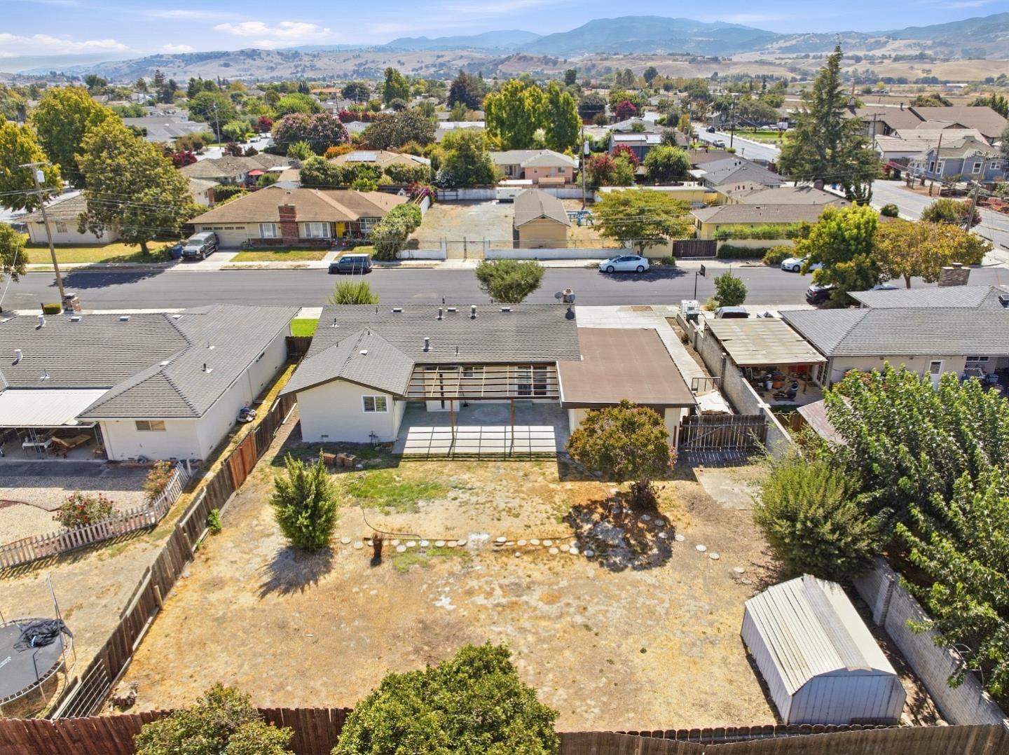 Aerial view of a home with a large fenced backyard, detached shed, and distant hills.