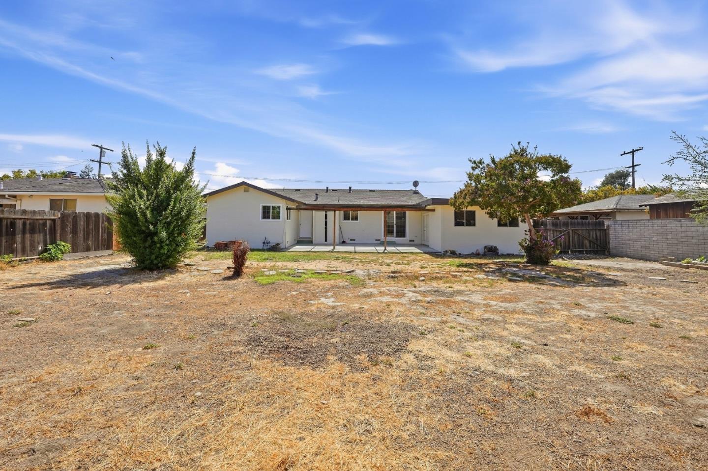 Single-story white home with a covered patio facing a large, mostly bare backyard.
